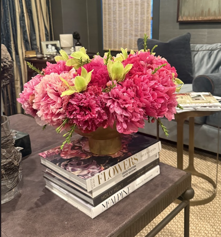 A large bouquet of pink and green flowers in a vase on top of three fashion and interior design books on a table in a cozy living room.