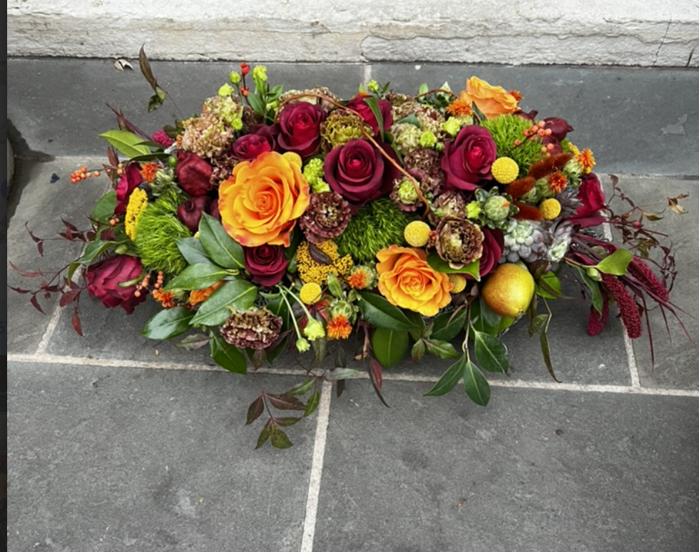 Colorful flower arrangement with roses, greenery, and small decorative elements on a tiled floor.