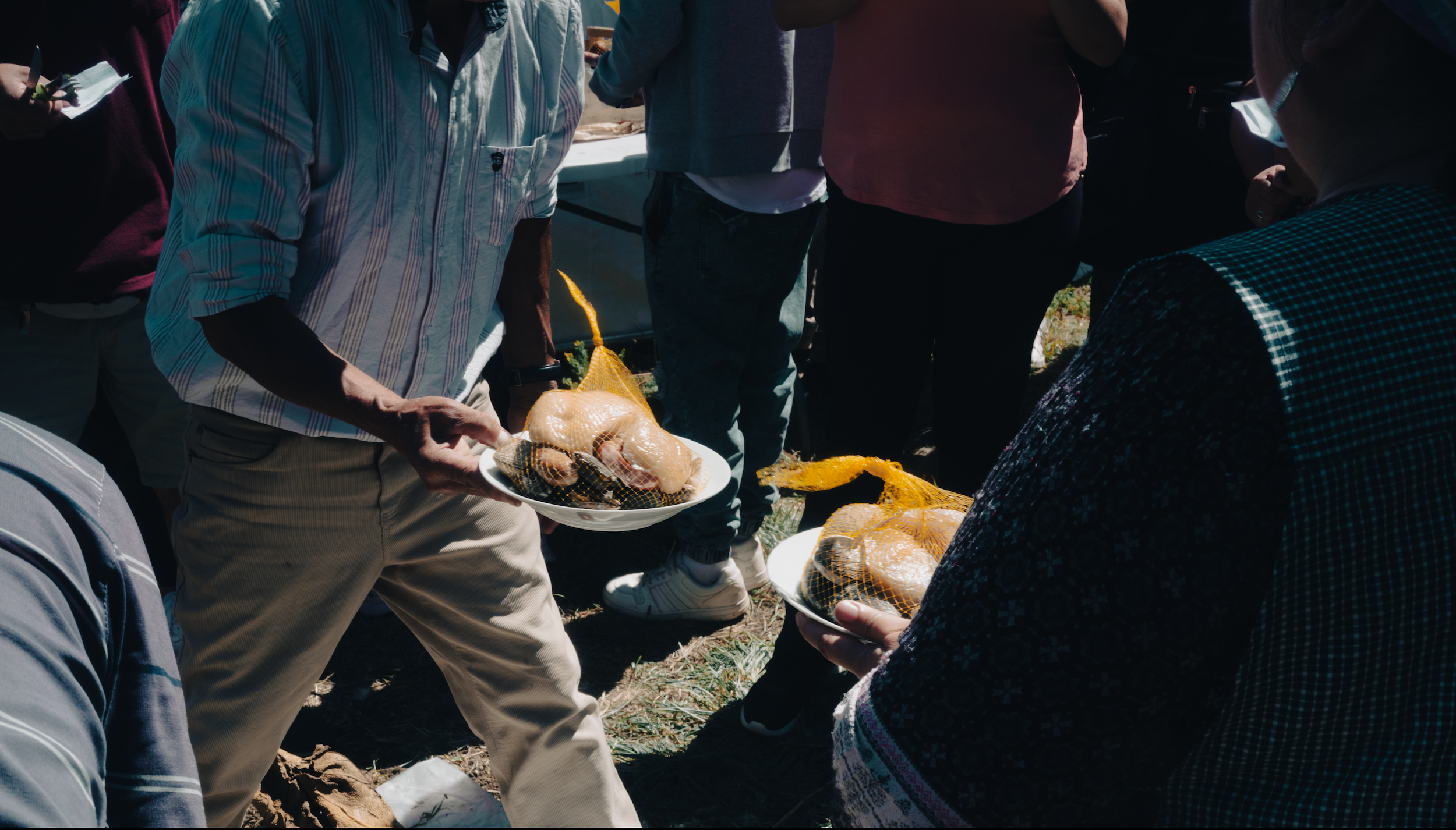 People gathered outdoors, with some holding plates of raw chicken covered in netting, likely at a poultry or food event.