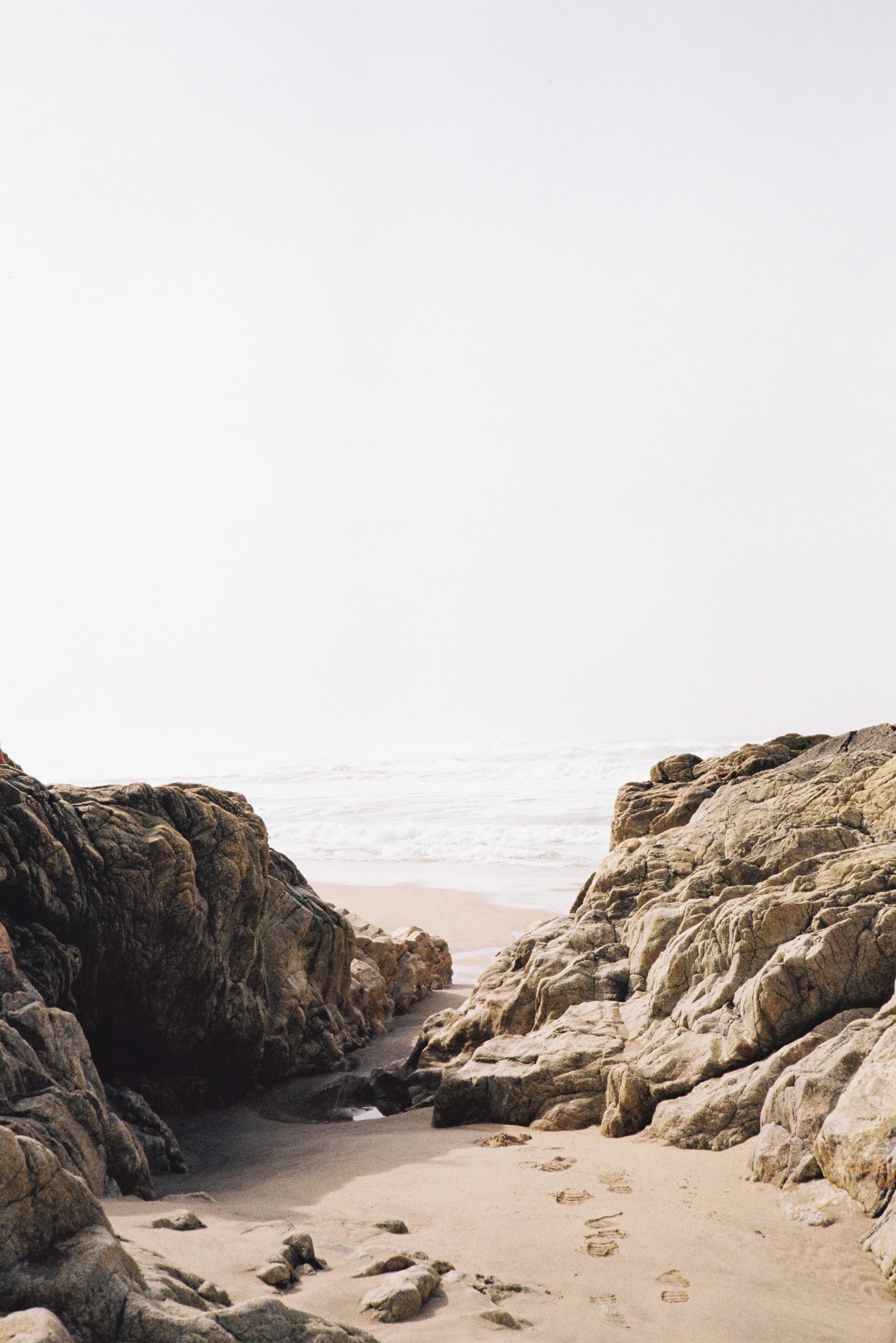 A beach scene with large rocks leading to the ocean on a cloudy day. Portugal.