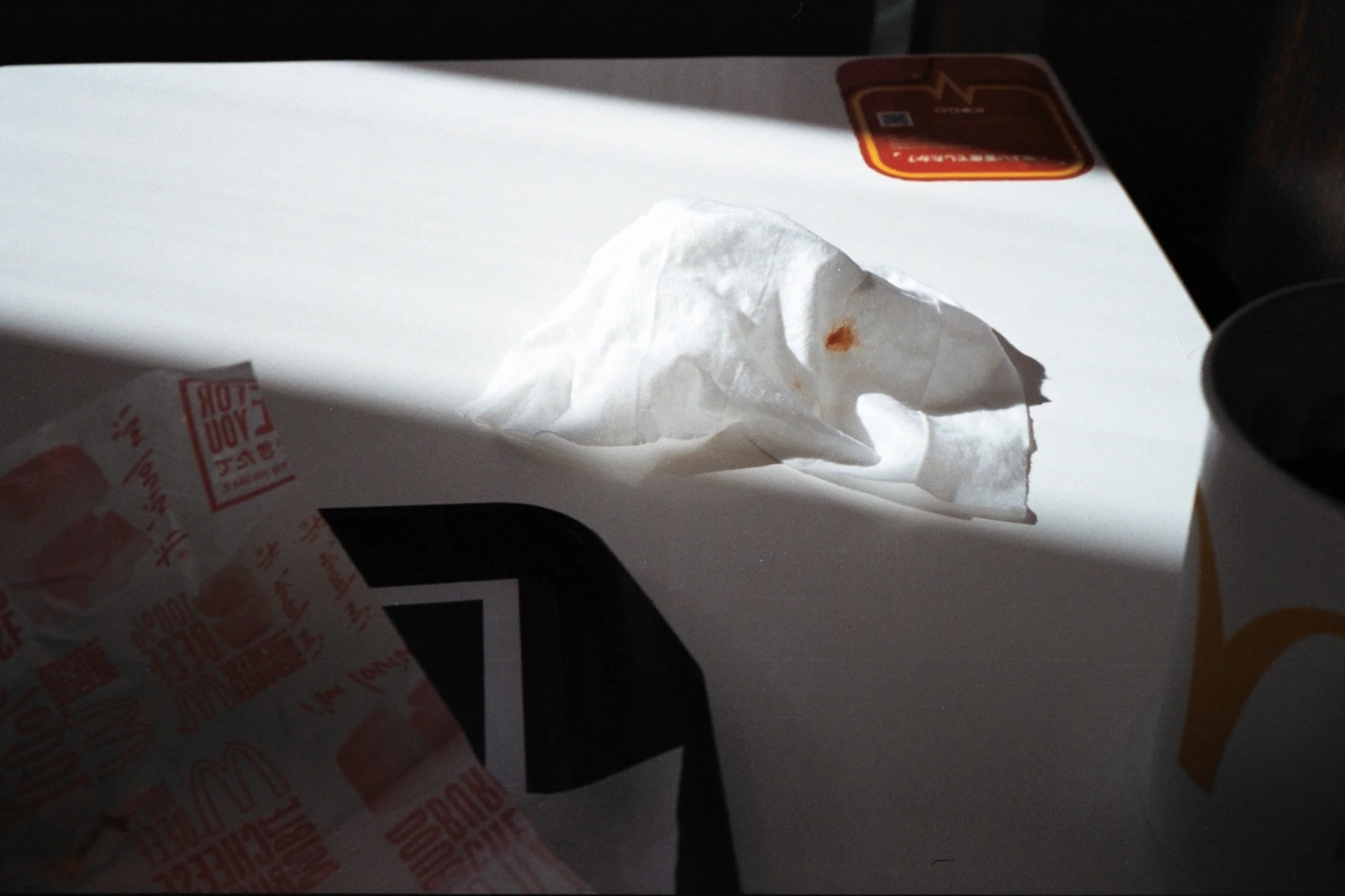 A crumpled napkin with a small stain, a McDonald's drink cup, and a ketchup packet on a white table.