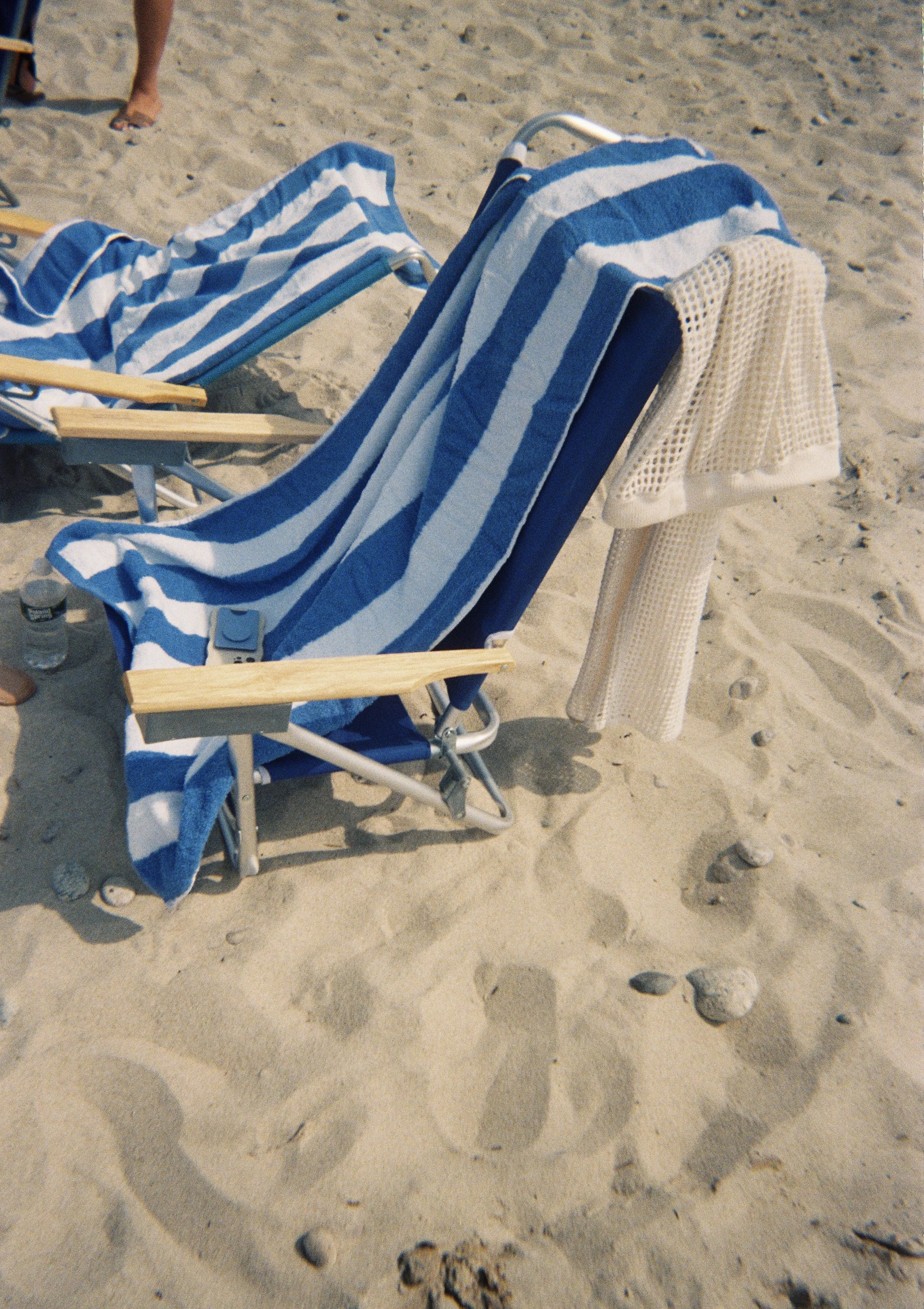 Beach chairs with blue and white striped towels and a beige cover-up on sandy beach