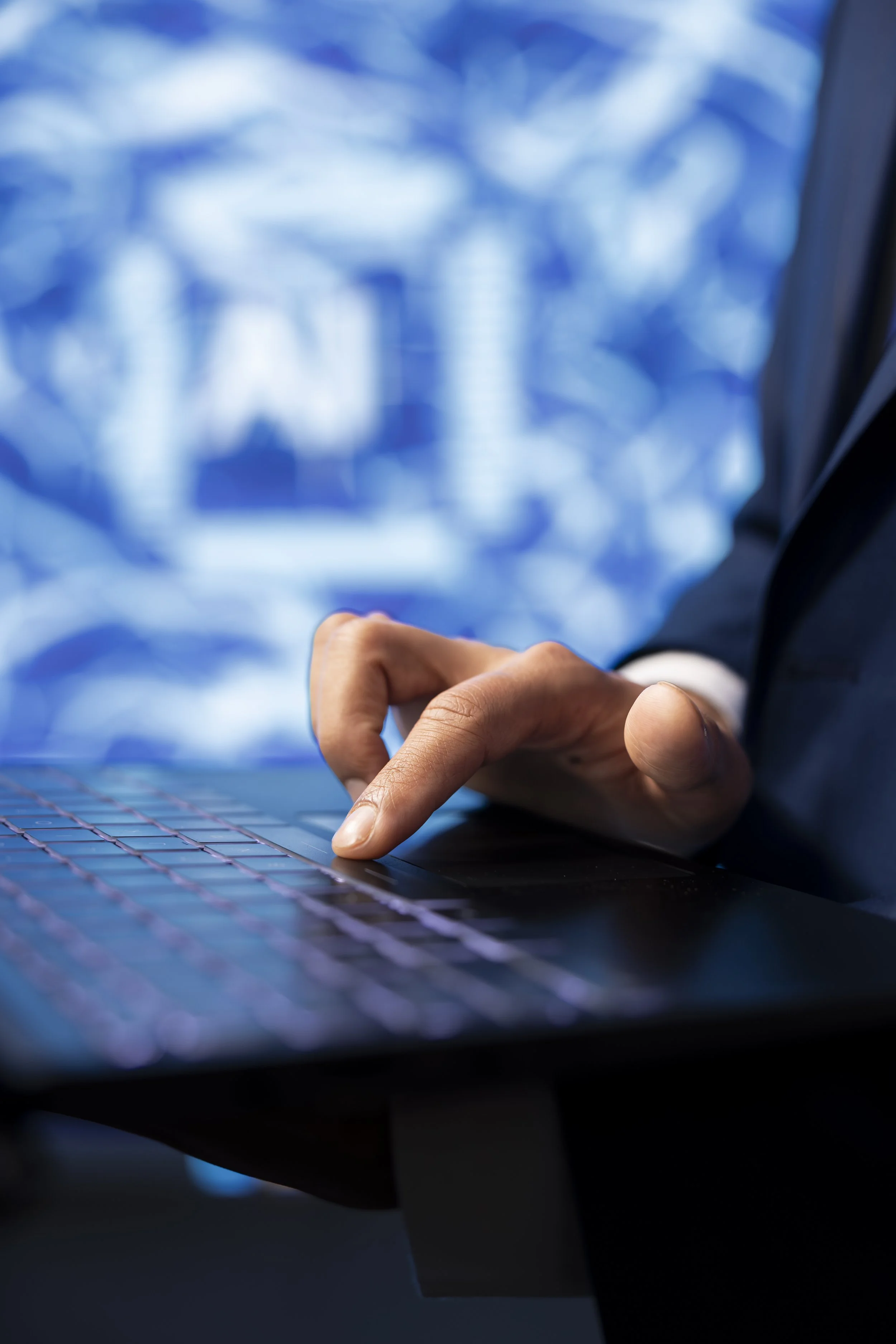 Close-up of a person's hand using a laptop keyboard with a blurred background of a cityscape on a digital screen.