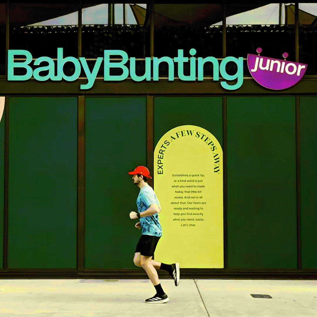 A man jogging past a retailer called Baby Bunting Junior, with a large yellow informational sign on the window.