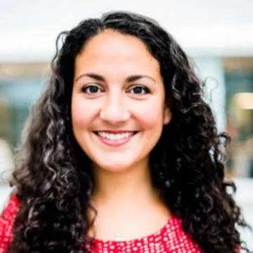 A woman with curly dark hair smiling outdoors.