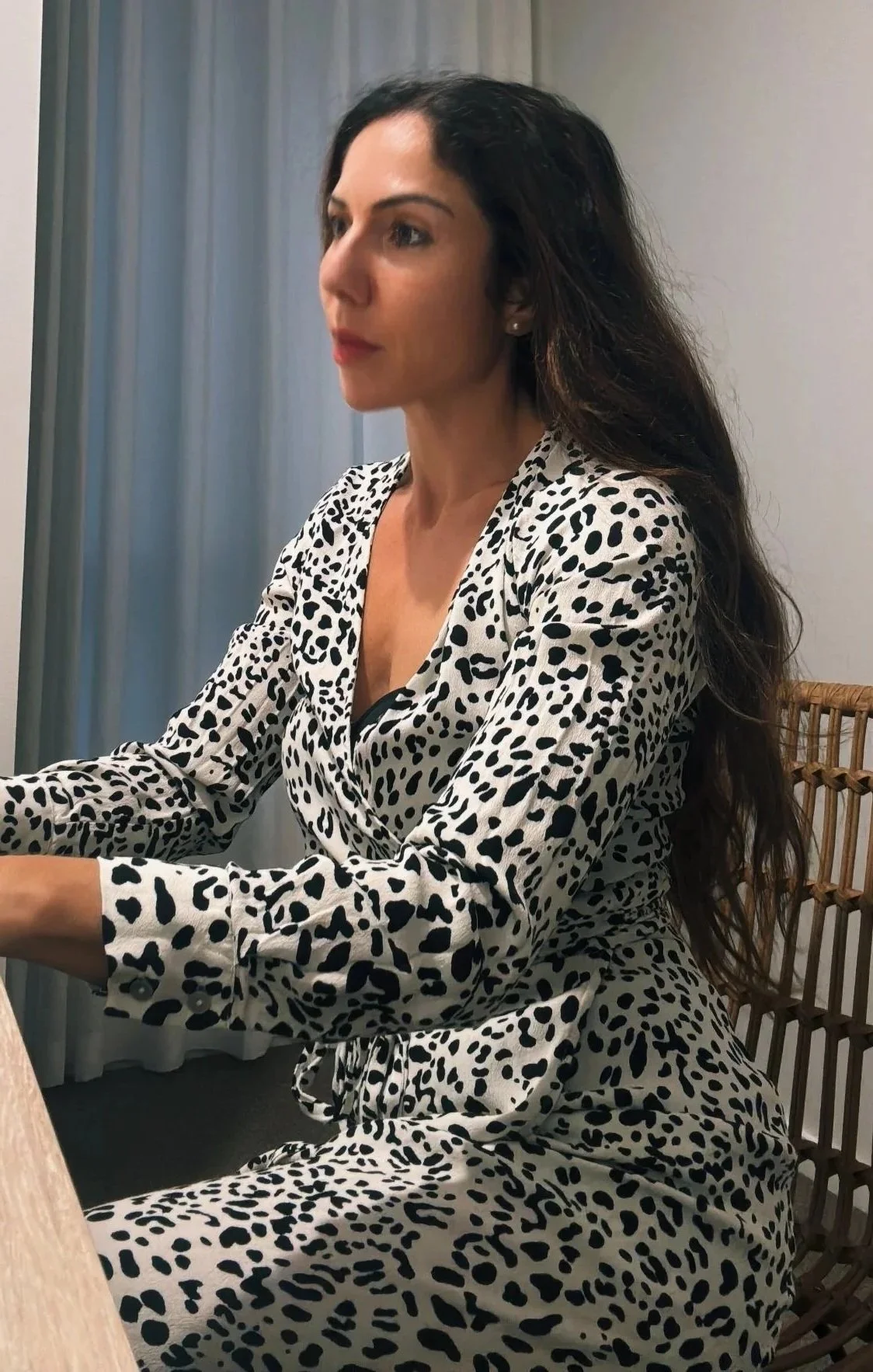 A woman with long dark hair wearing a white and black leopard print dress sitting at a table.