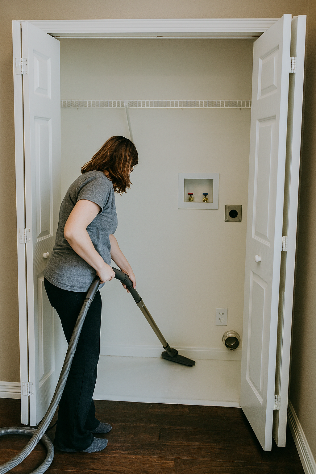 Woman cleaning the laundry area with a vacuum in a small laundry closet.