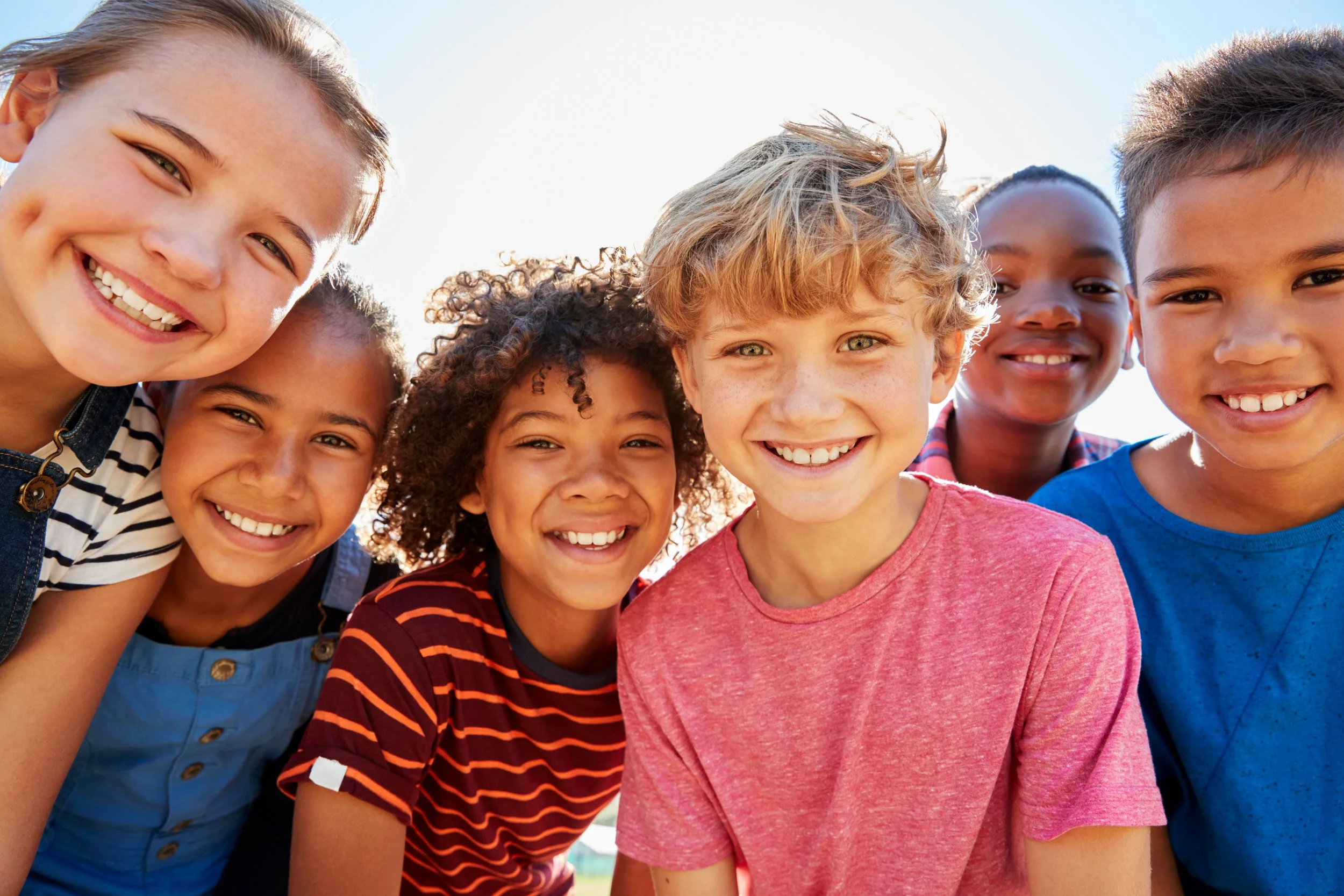 Group of smiling children close-up outdoors on a sunny day.