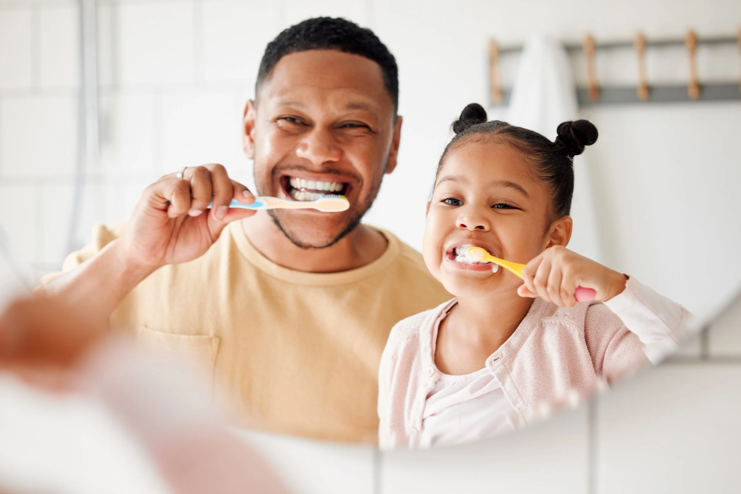 A man and a young girl brushing their teeth together in a bathroom.
