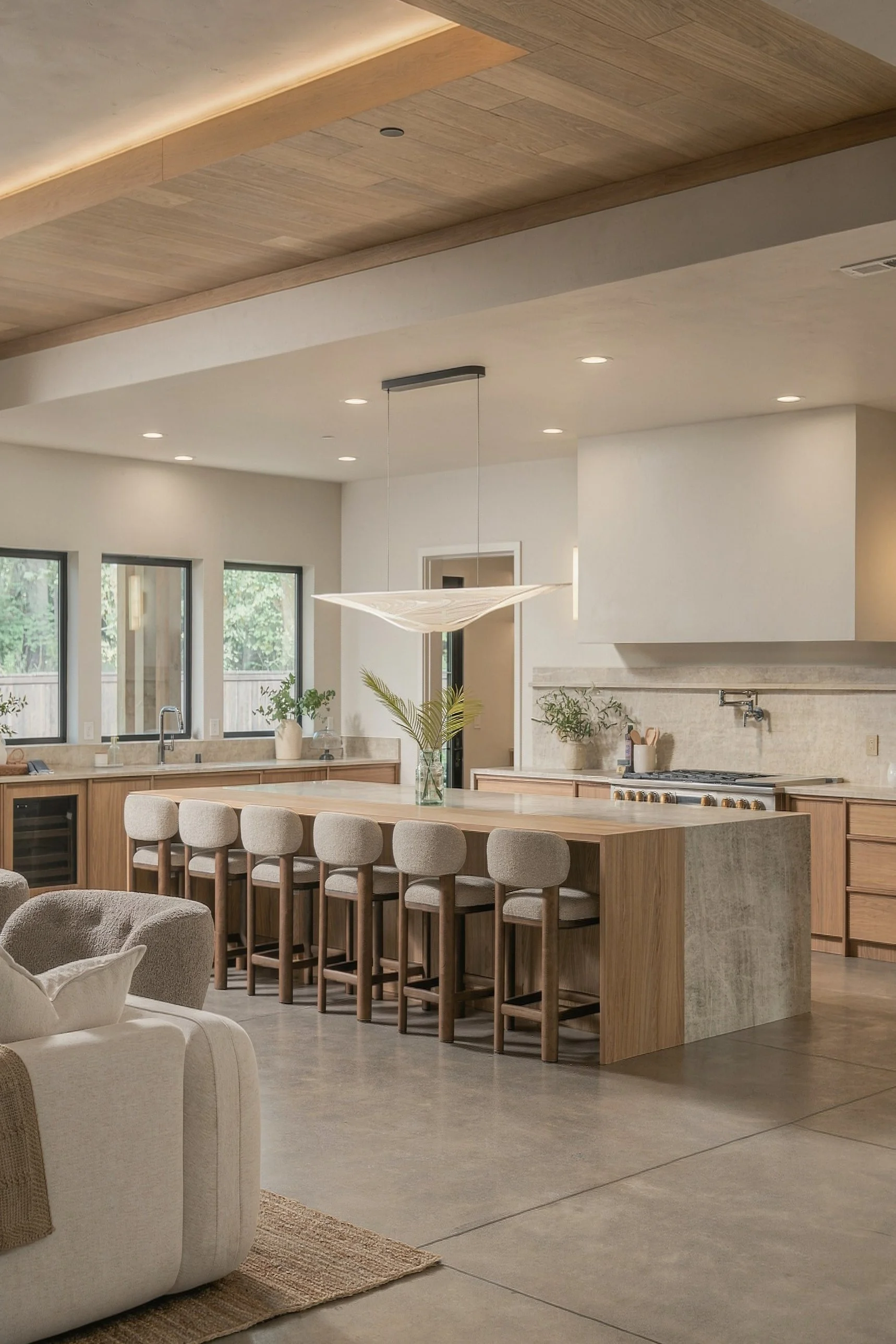 Oak and stone waterfall island with six stools under a sculptural pendant