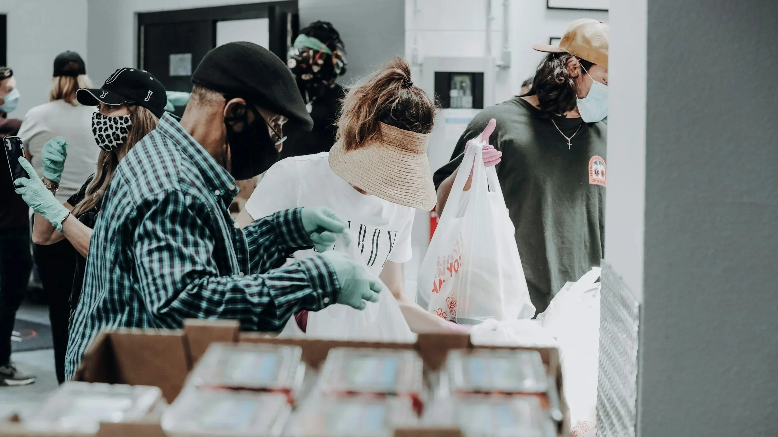 People wearing masks and gloves at a food distribution table, organizing and handing out food packages.