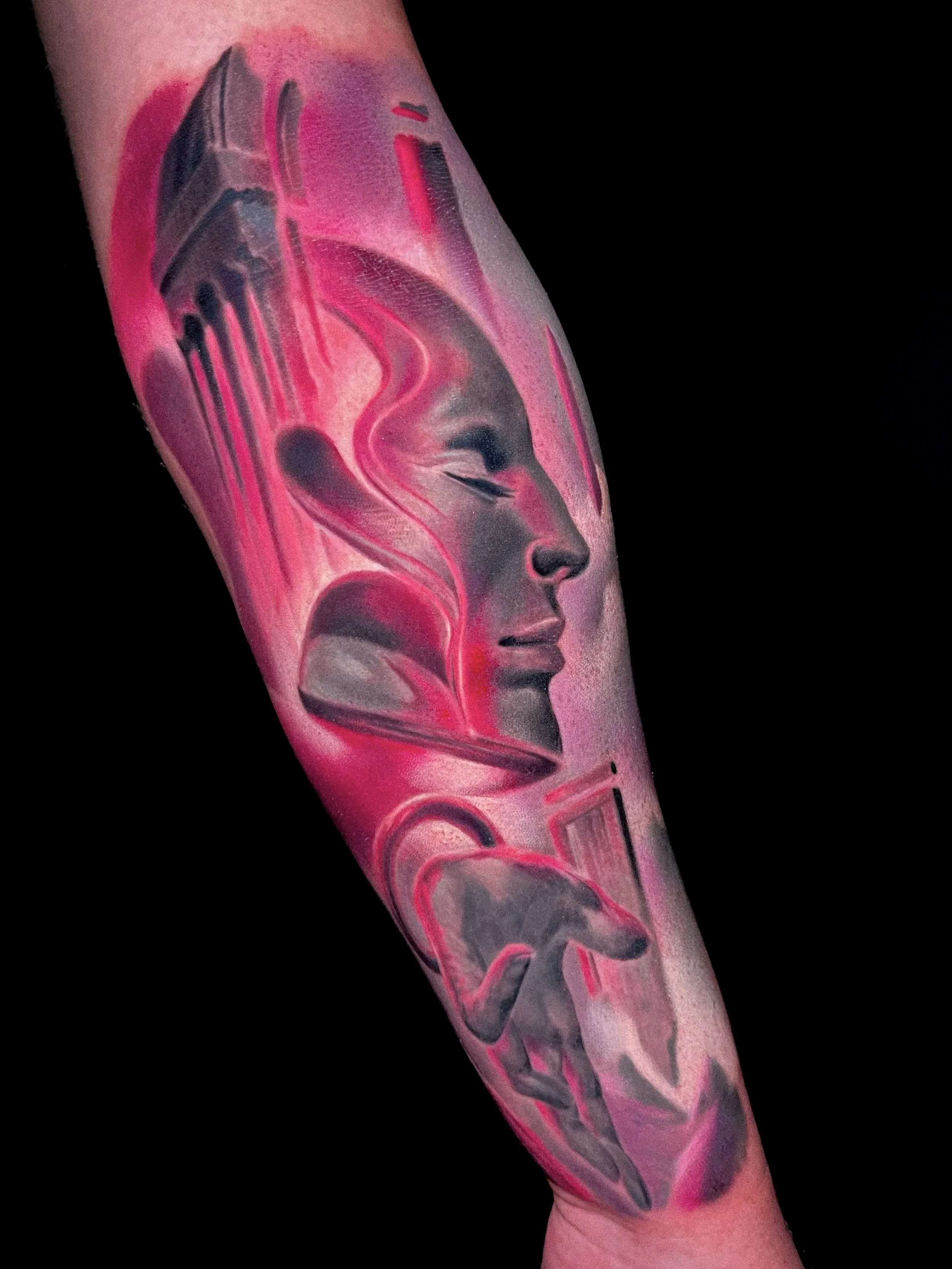 Tattoo of a woman's face in profile with red and black abstract elements on an arm against a black background.