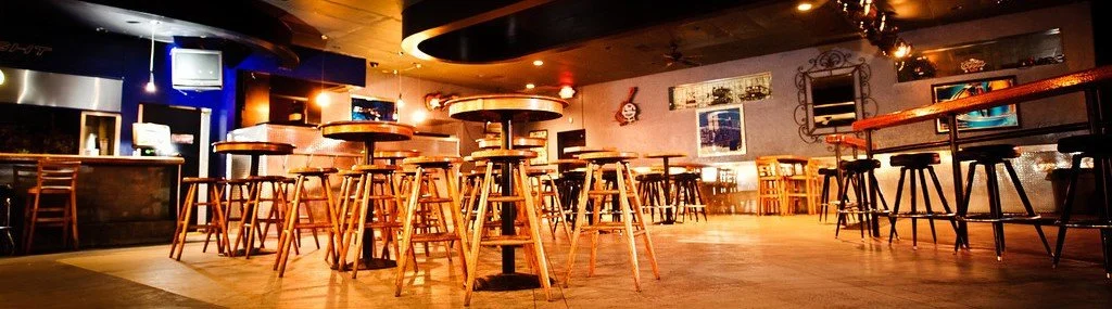 Empty bar or pub with high tables and bar stools, warm lighting, and wall decorations.