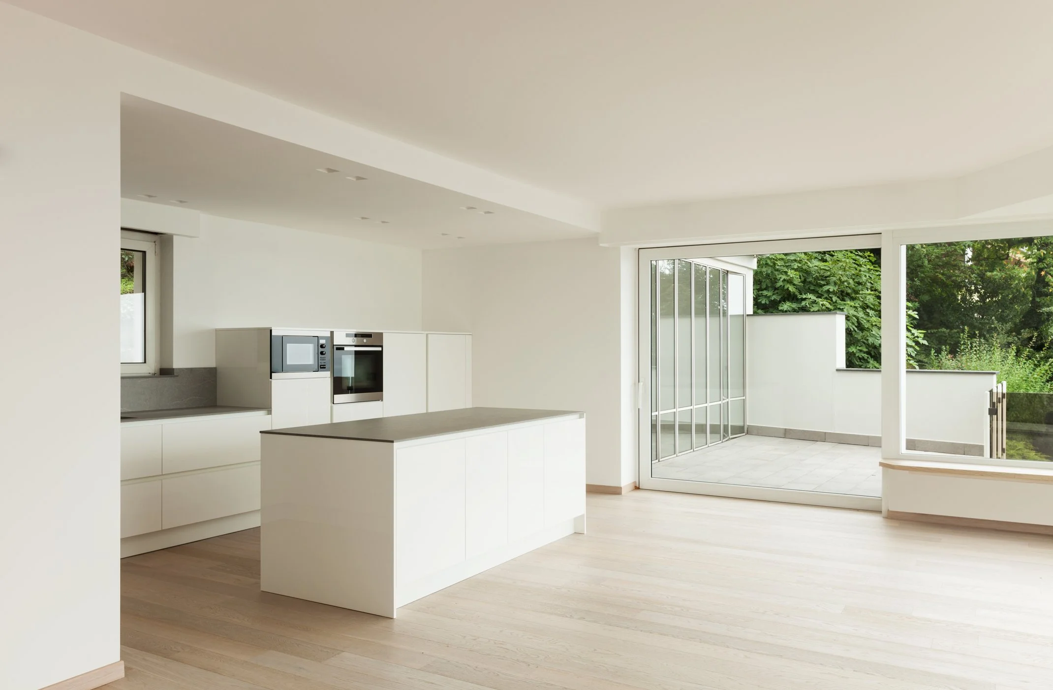 Modern suburban house with a gray garage door, a landscaped front yard with green grass and desert plants, and a gravel driveway under a clear blue sky.