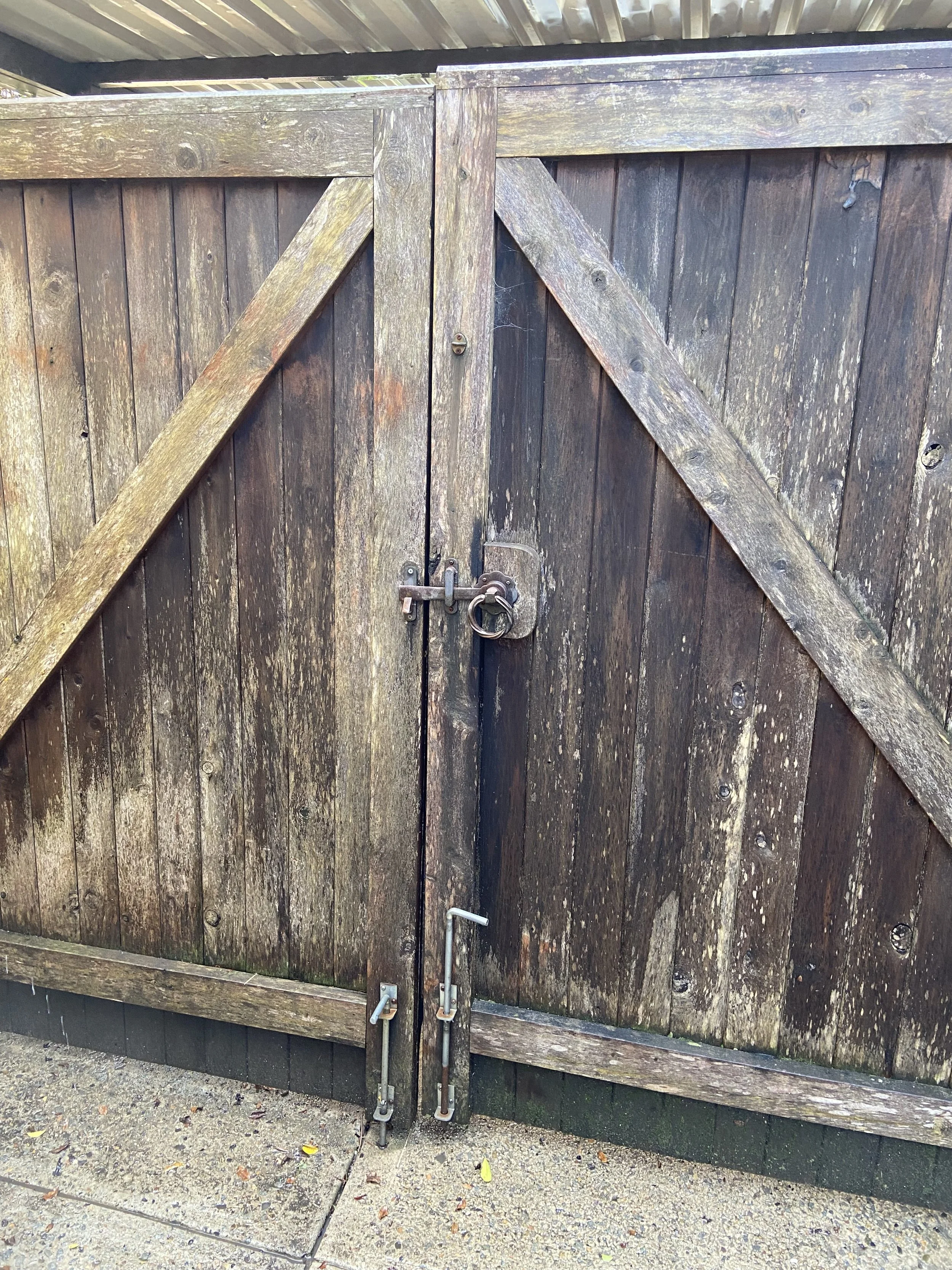 Wooden gate with metal lock and hinges, weathered surface, on concrete ground.