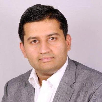 A man with dark hair in a gray suit and white shirt.