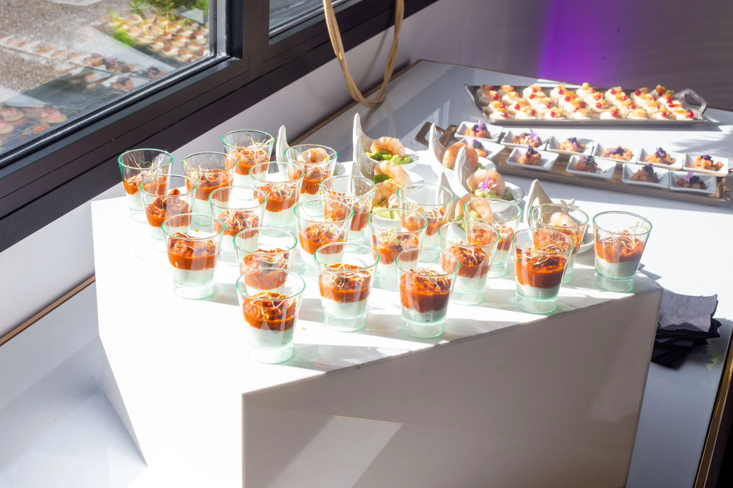 Plateau de verrines avec une couche de crème et un coulis de tomate, desserts en arrière-plan sur des plateaux