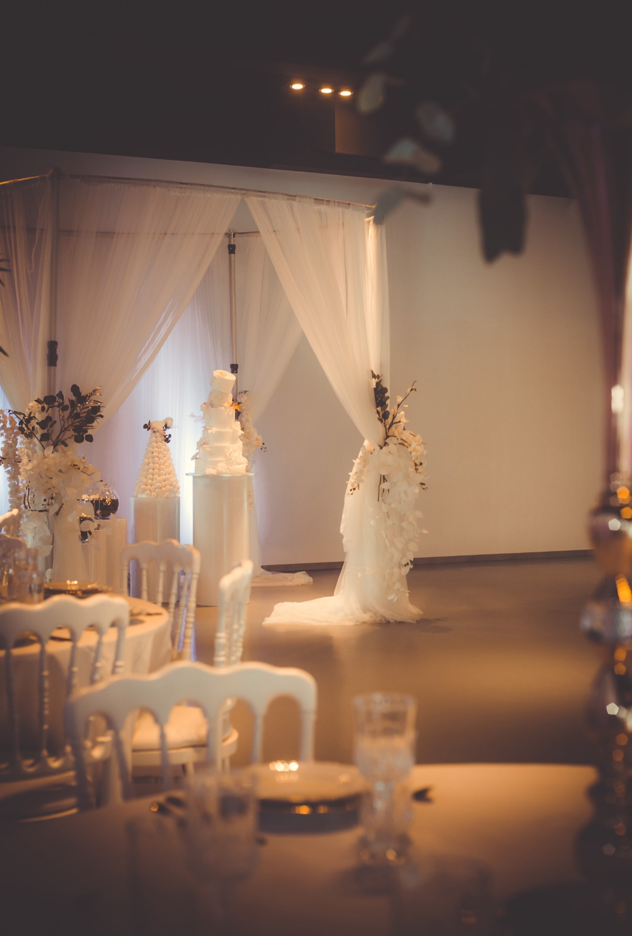 Décor de mariage avec un gâteau blanc, ornements floraux, et rideaux blancs derrière une scène principale