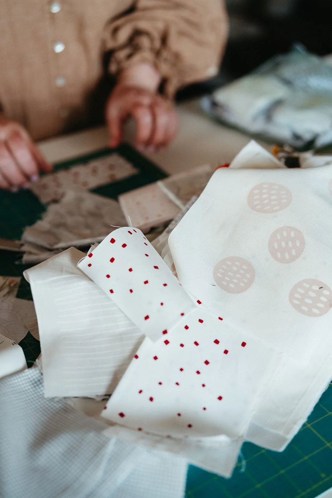 Close-up of crumpled paper napkins with red polka dots and white stripes, on a fabric surface with background of a person's hands and sewing tools.