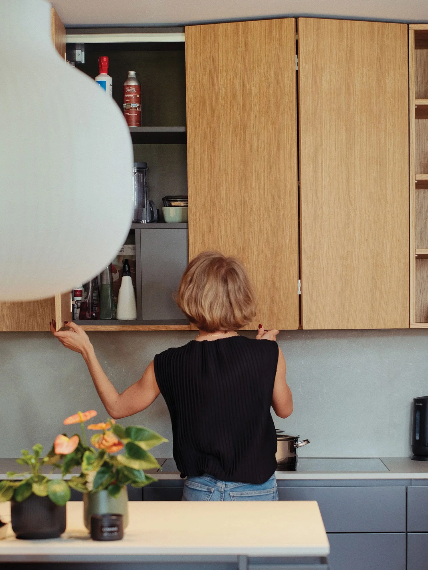 Oseba odpira omarice v kuhinji v temno sivi in naravnem lesu.