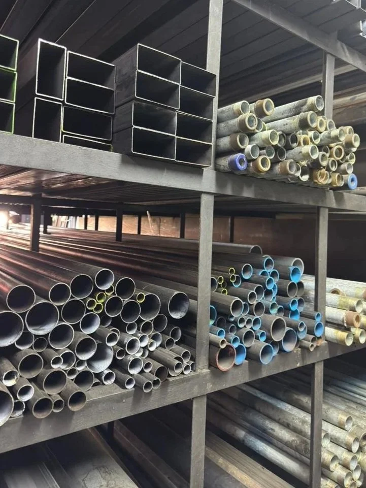 Industrial metal pipes and rectangular tubing arranged on metal shelving in a warehouse.
