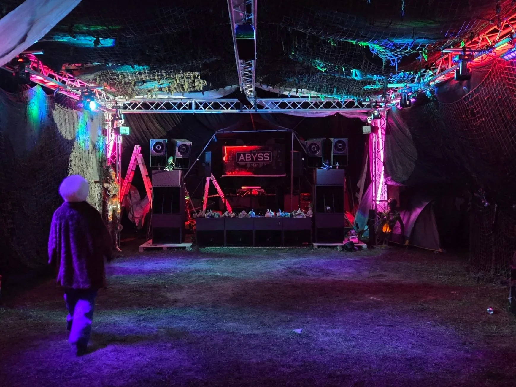 An empty dance club with colorful lighting, black netting on the ceiling, and a DJ booth at the center labeled 'ABYSS'.