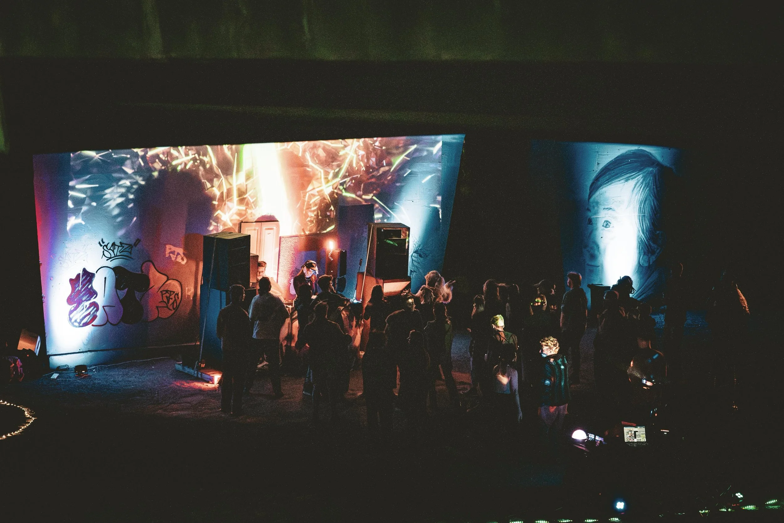 An indoor music event with a crowd gathered in front of a stage featuring colorful lights, graffiti art, and large Chinese art images projected on the wall.