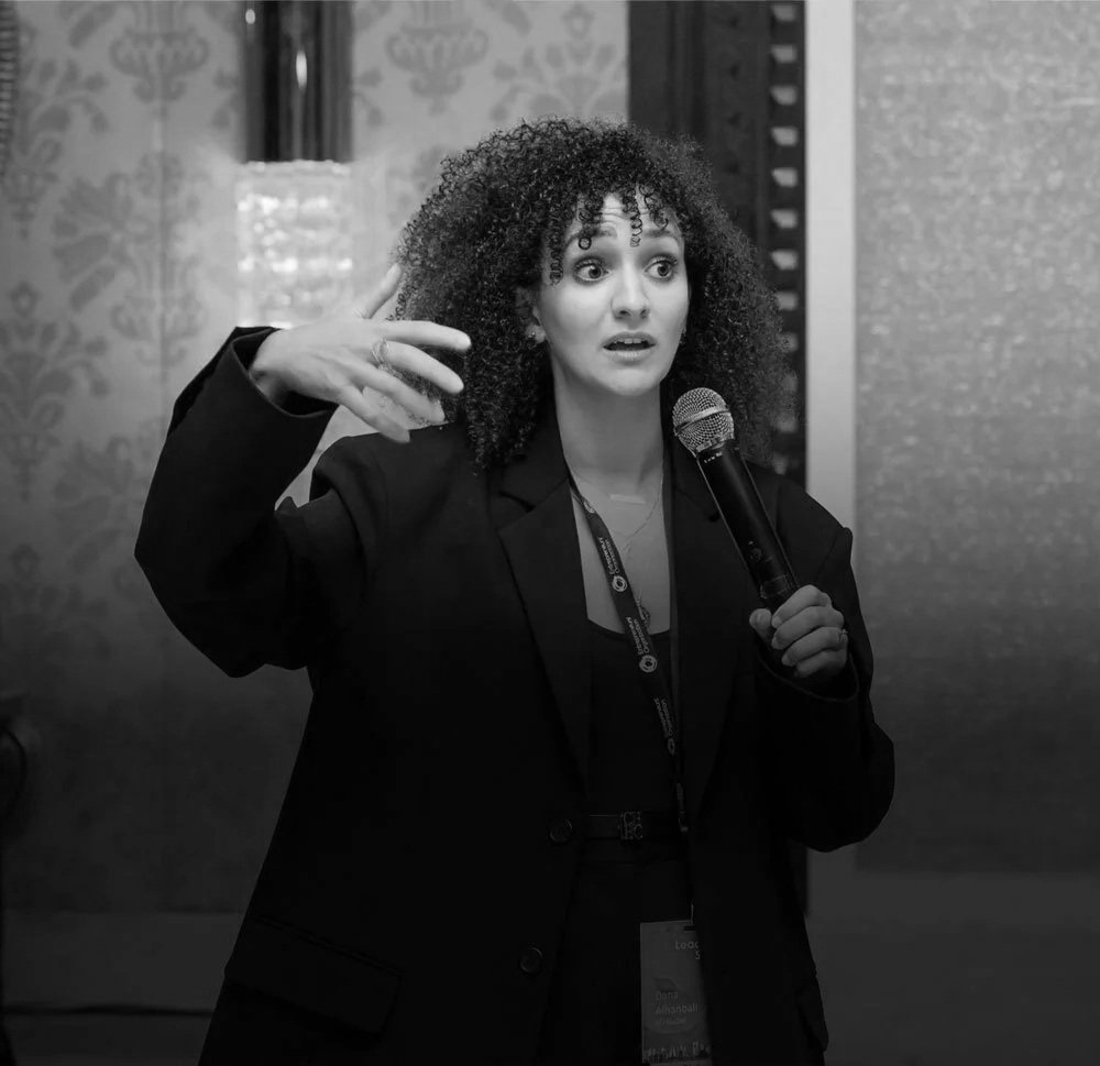 A woman with curly hair speaking into a microphone during a presentation or speech.