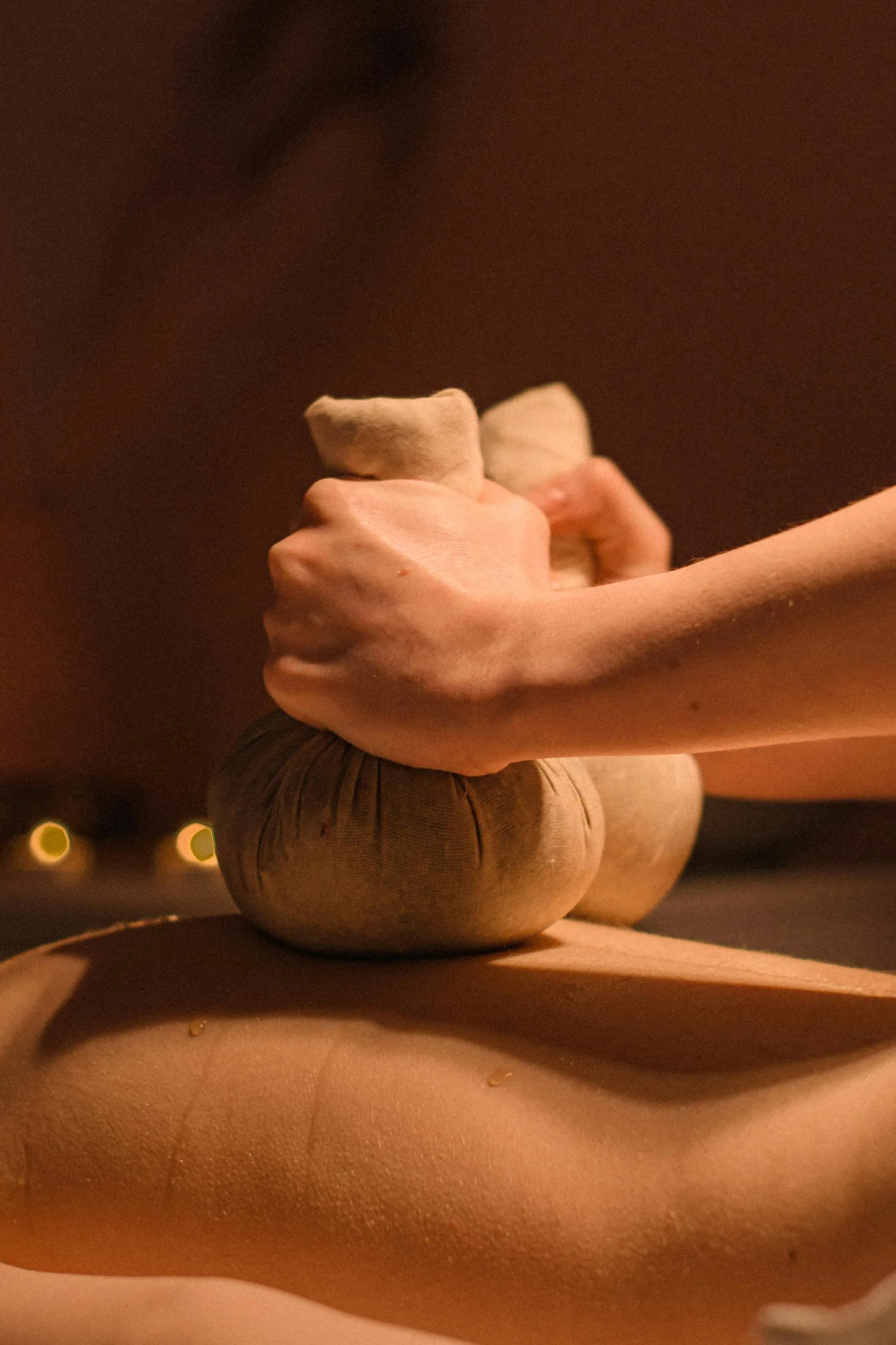A person performing a hot stone massage, with warm stones stacked on their back and hands applying pressure.