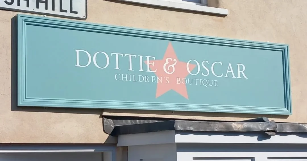 Store sign for 'Dottie & Oscar Children's Boutique' on a light-colored building