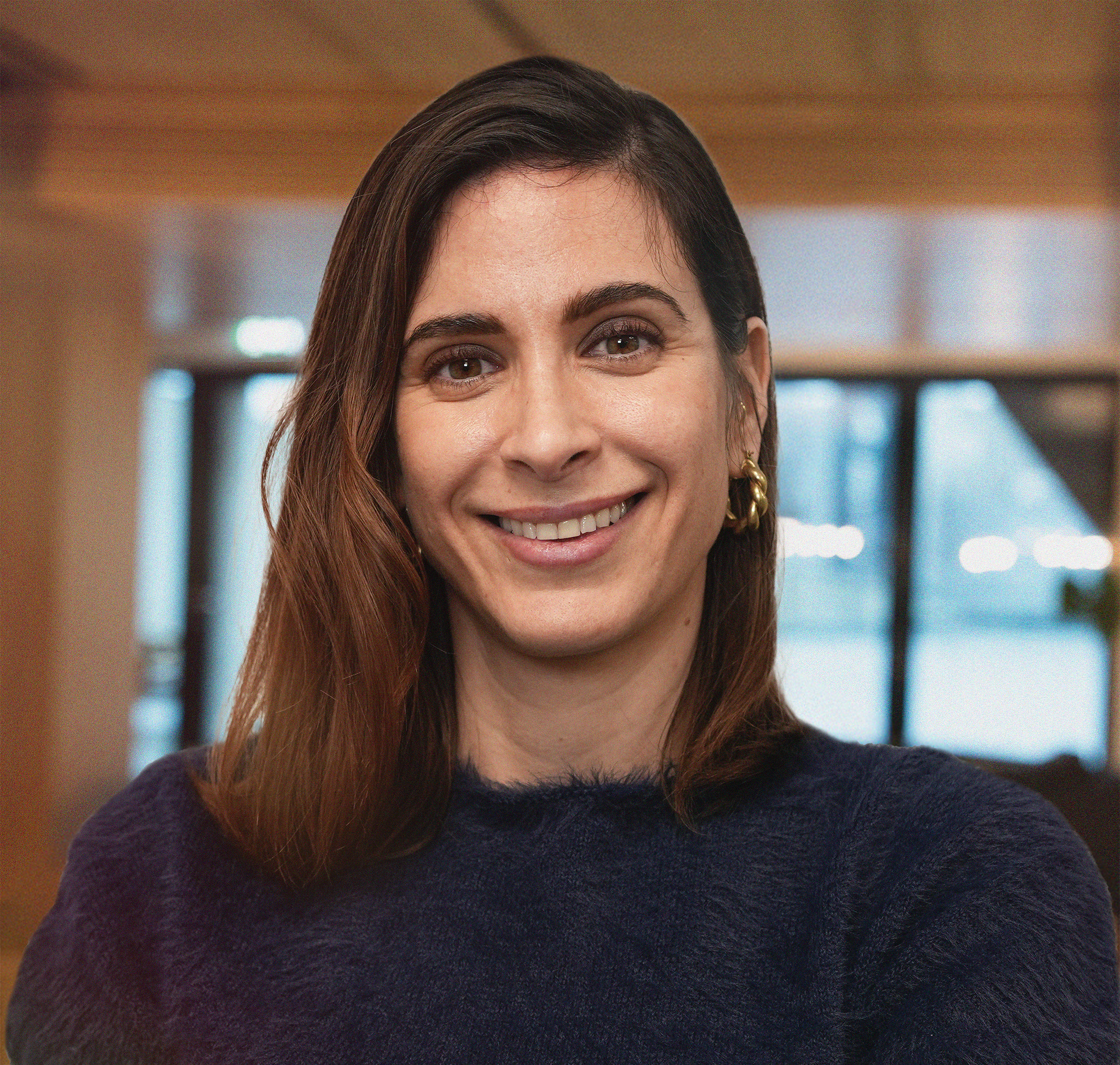 Black and white portrait of a smiling woman with shoulder-length hair, wearing a dark turtleneck sweater, with her arms crossed, against a plain light background.