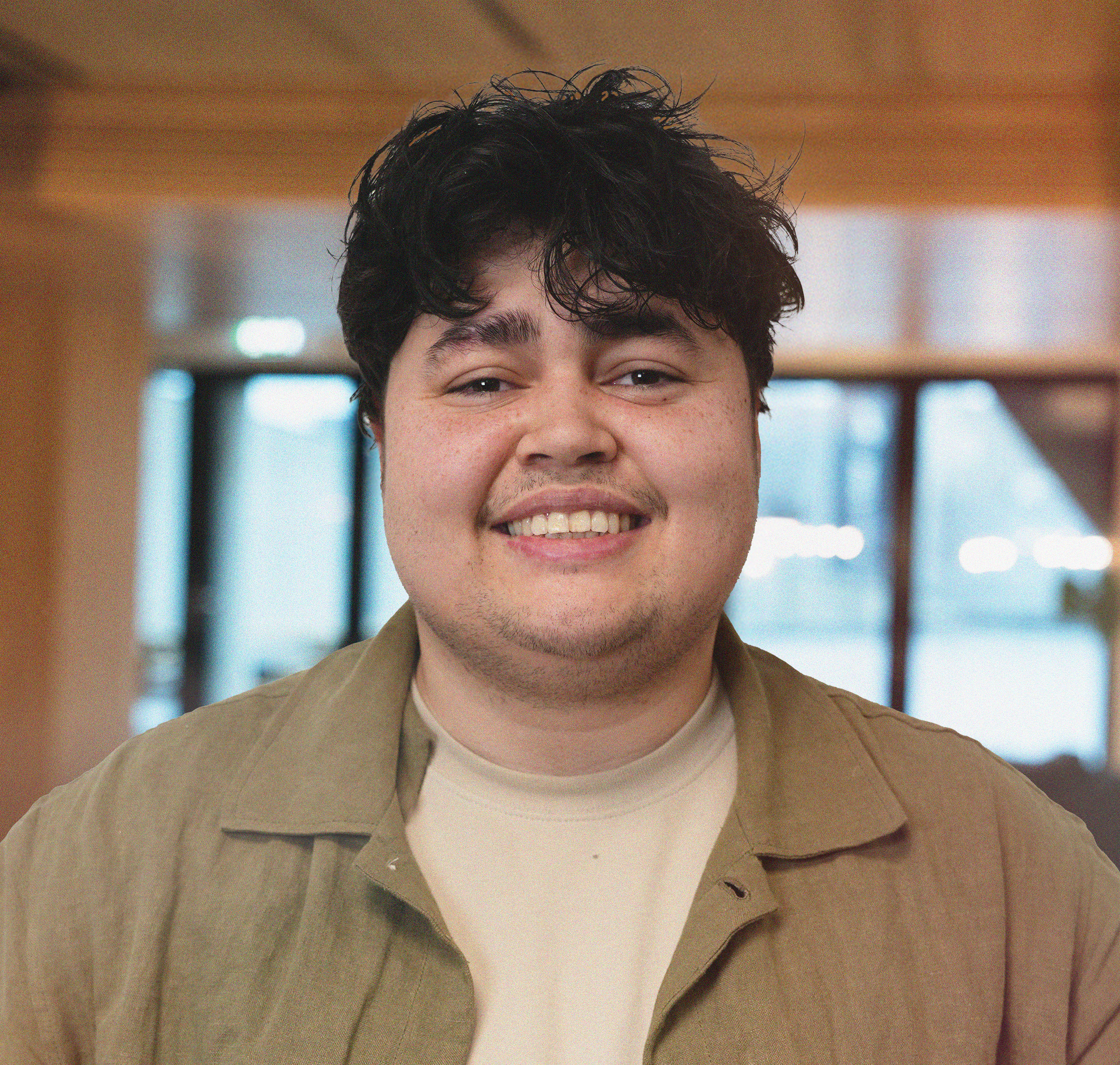 Black and white close-up portrait of a young man with wavy hair wearing a white t-shirt, looking directly at the camera with a neutral expression.