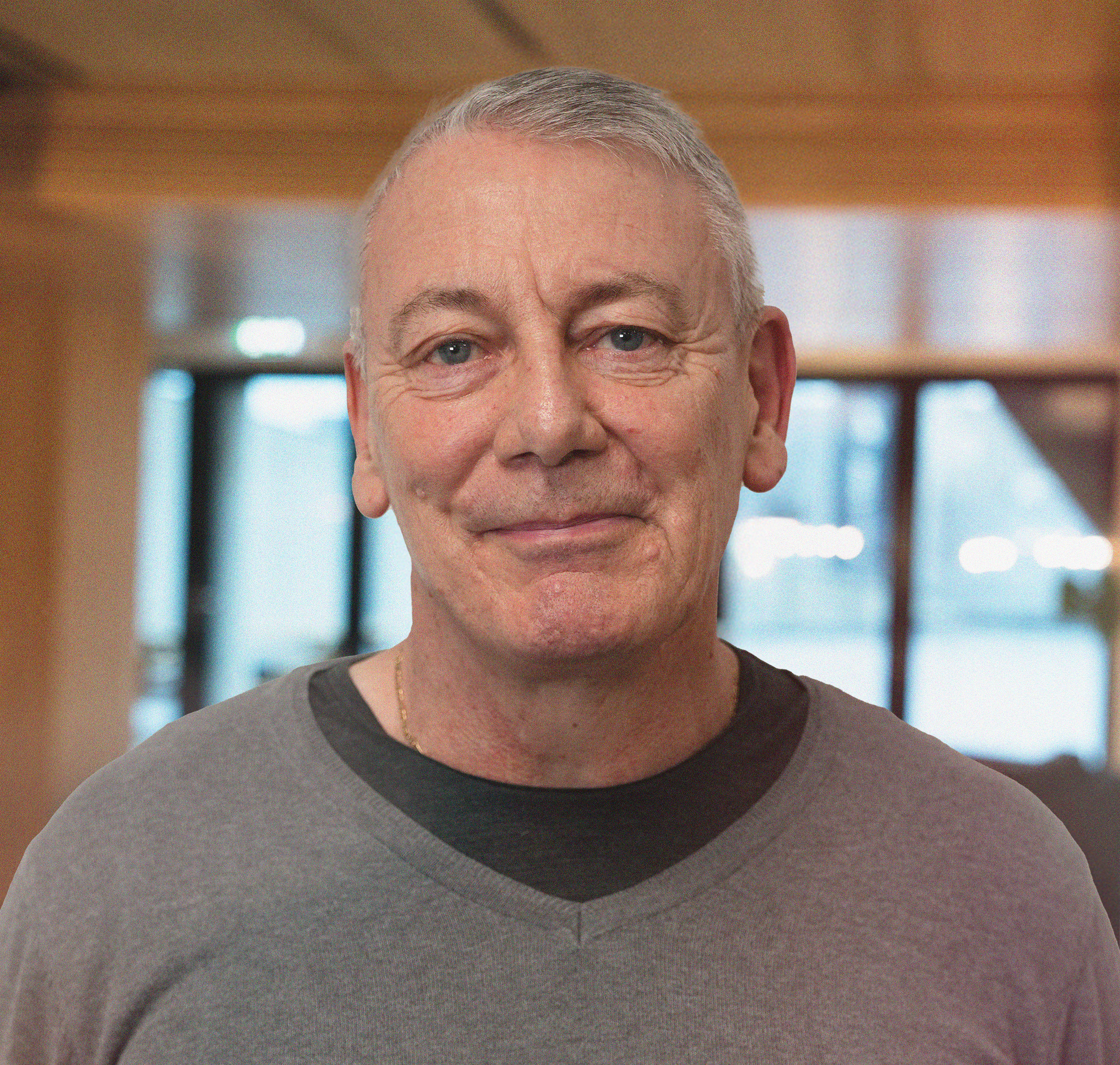 Et svart-hvitt bilde av en mann med kort, grått hår, iført en svart genser, som smiler svakt mot kameraet.