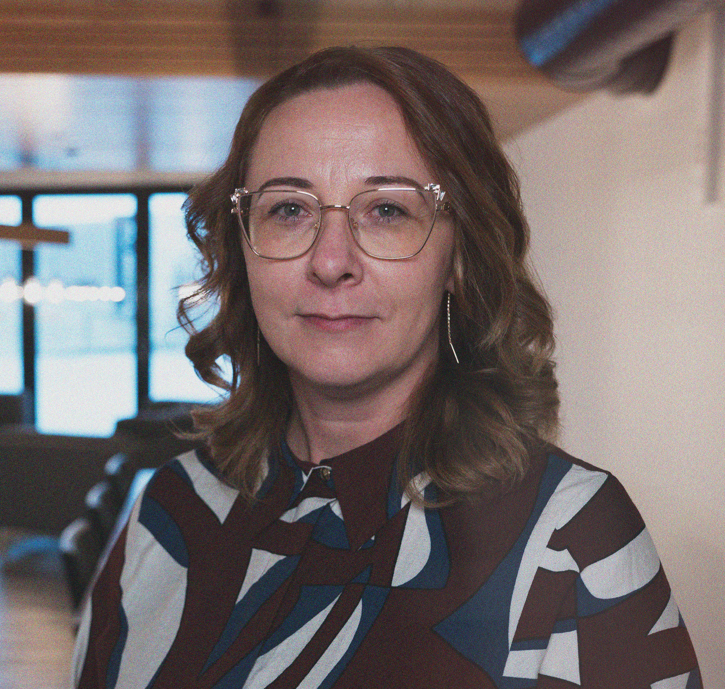 Portrett av en kvinne med briller, kort kastanjefarget hår, iført en sort topp og en mønstret sjal rundt halsen, tatt i svart-hvitt.