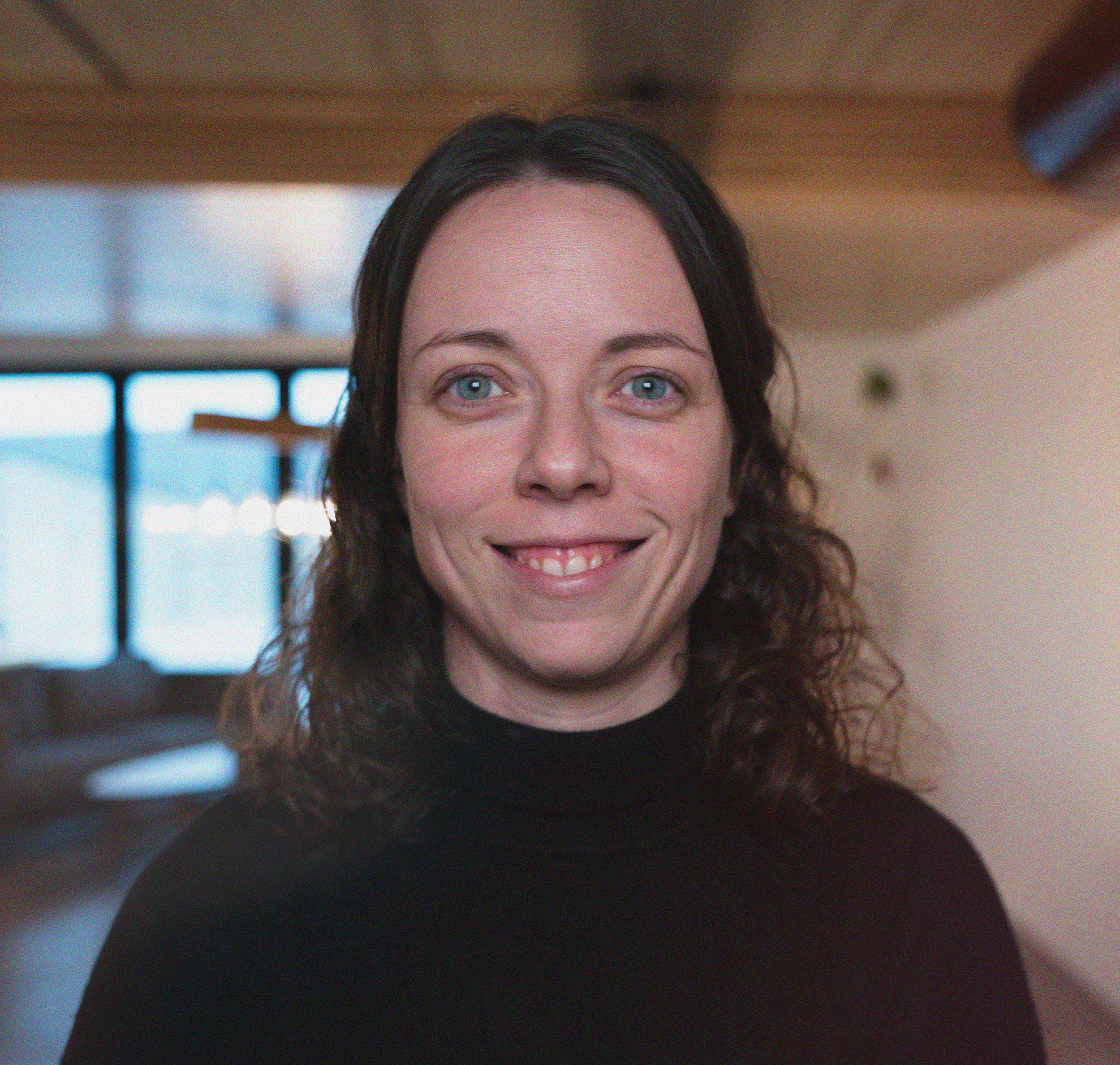 Black and white photo of a woman with shoulder-length curly hair, wearing a button-up shirt, smiling with arms crossed