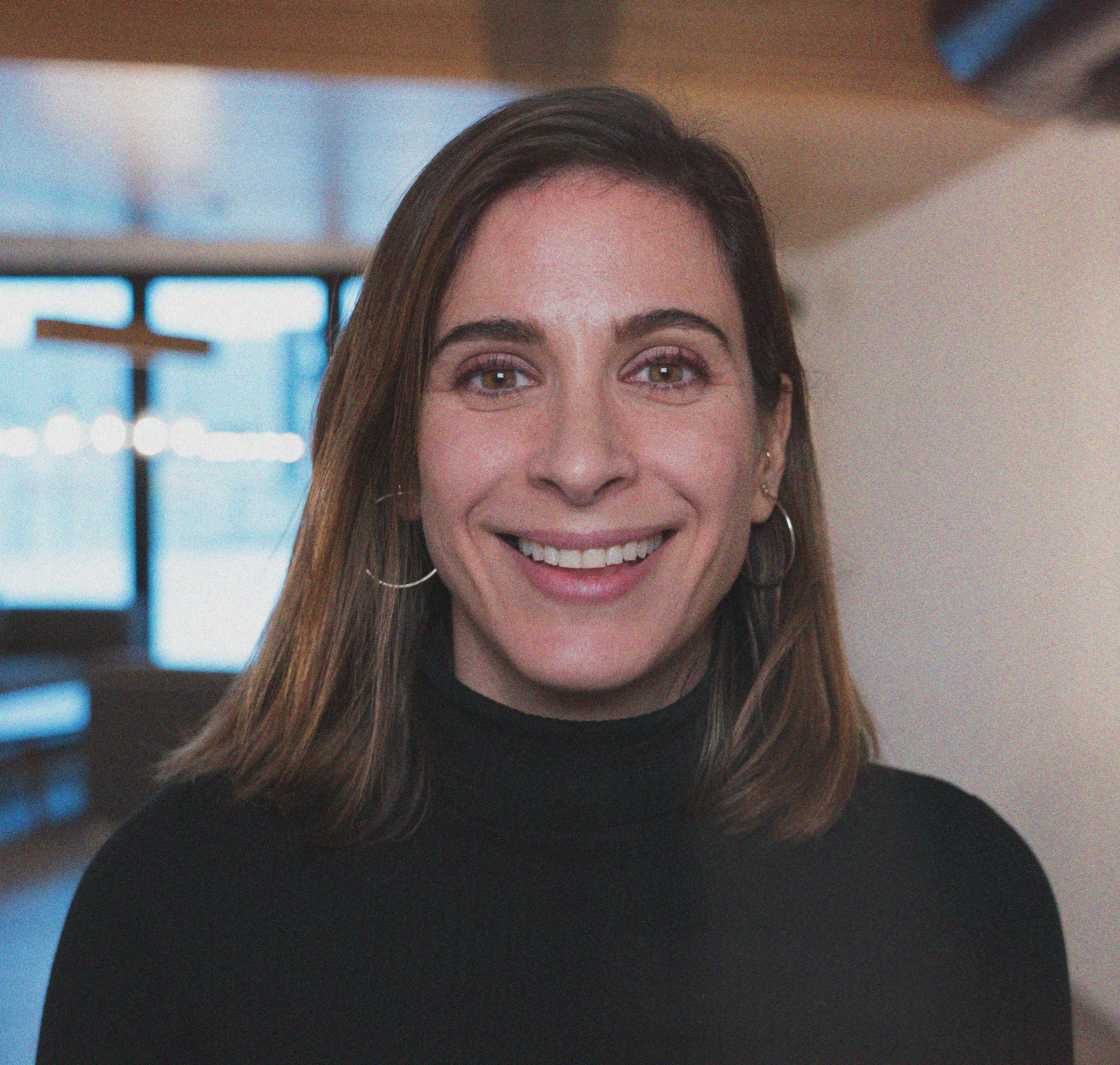 Black and white portrait of a smiling woman with shoulder-length hair, wearing a dark turtleneck sweater, with her arms crossed, against a plain light background.