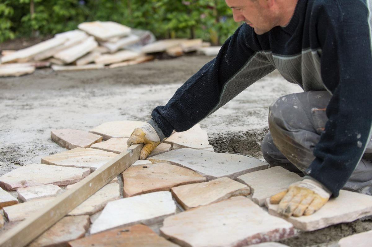 Ein Arbeiter verlegt eine Stein- oder Terrassenmauer im Freien auf einer Baustelle.