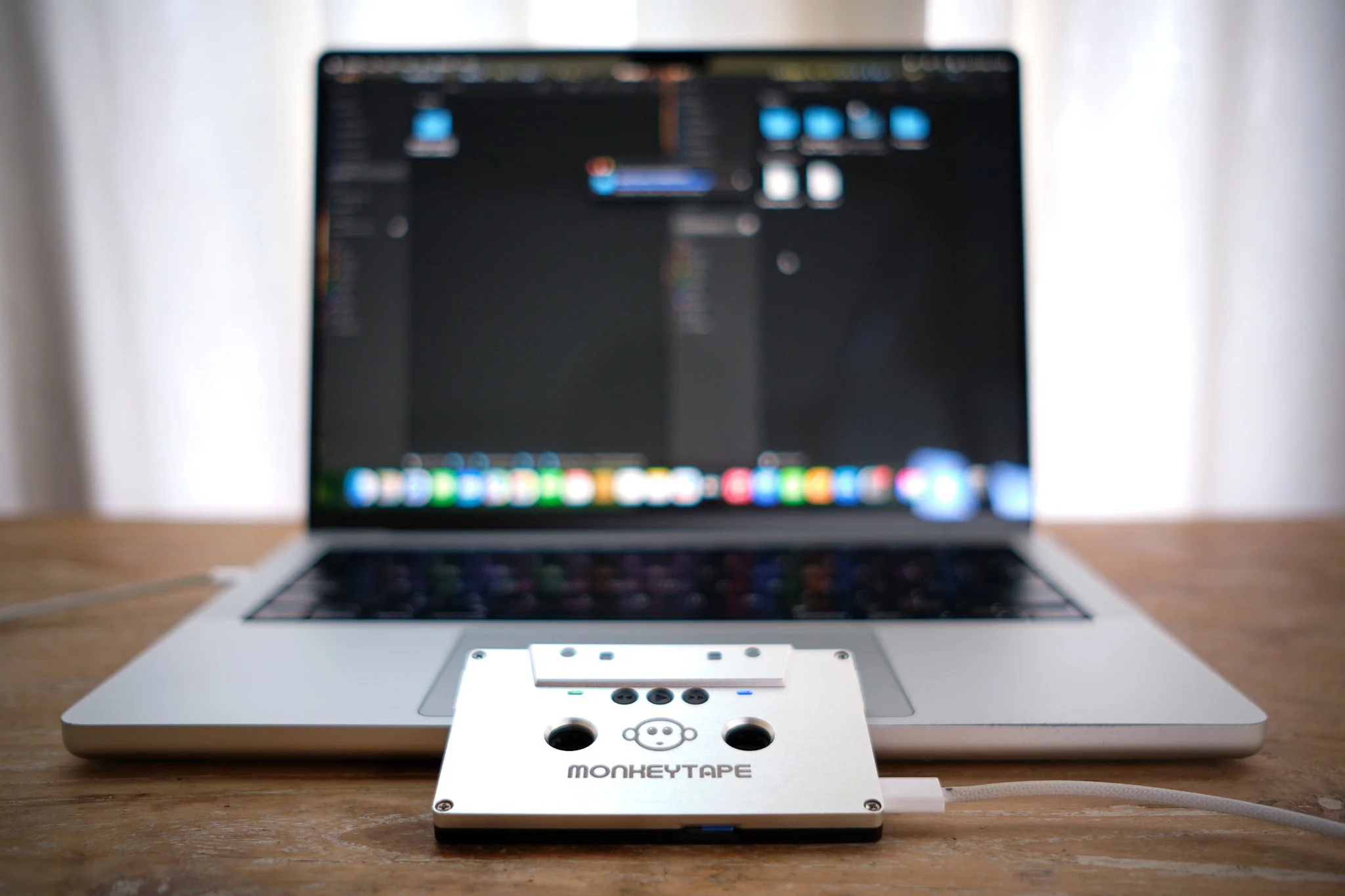 A laptop connected to a tape recorder on a wooden desk.