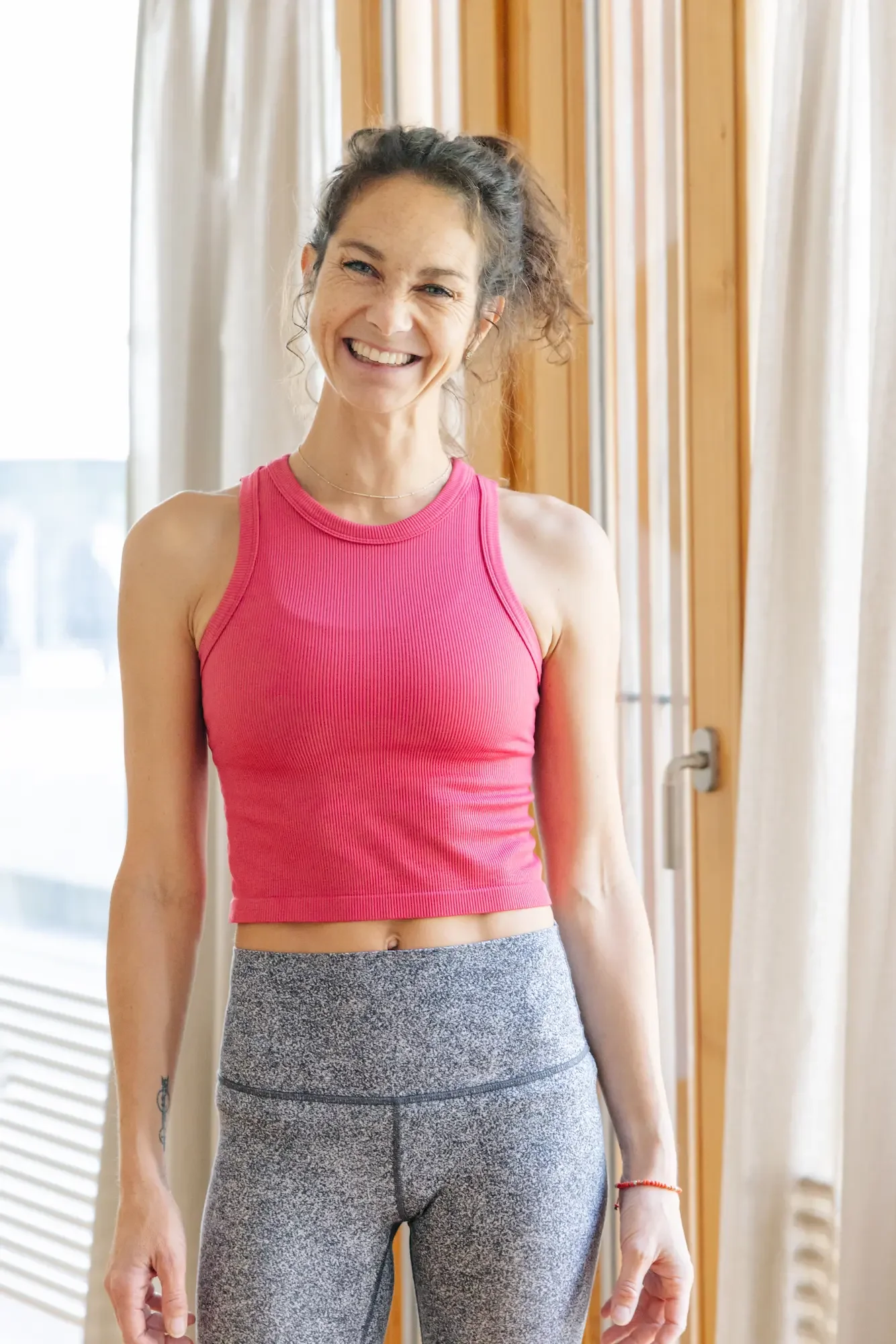 Porträt von Sarah, Gründerin von MindfulMama in Interlaken. Lachend und sympathisch im Yogaraum, trägt ein pinkes Top. Sportlich und natürlich – Rückbildungskursleiterin in Interlaken.