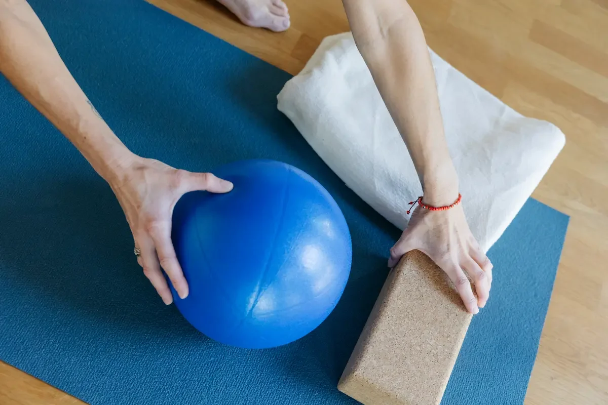 Jemand bereitet auf einer blauen Yogamatte einen Pilatesball, Yogablock und eine Decke für den Rückbildungskurs in Interlaken vor.