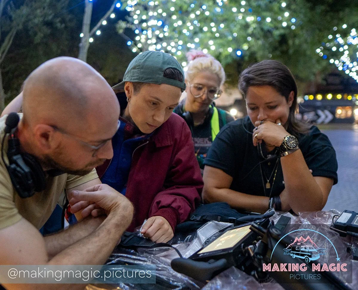 The MAGIC film crew gathered around outdoors at night, looking at the monitor. 