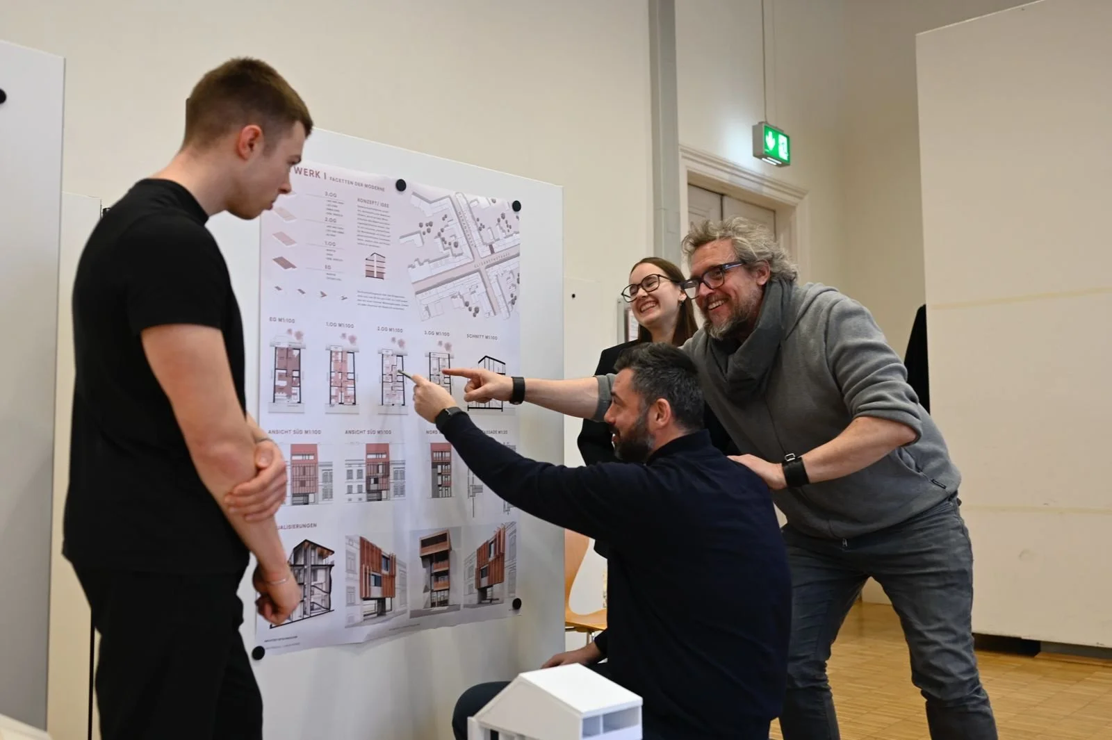 Five people discussing architectural designs and plans on a presentation board, with a small model of a building in the foreground.