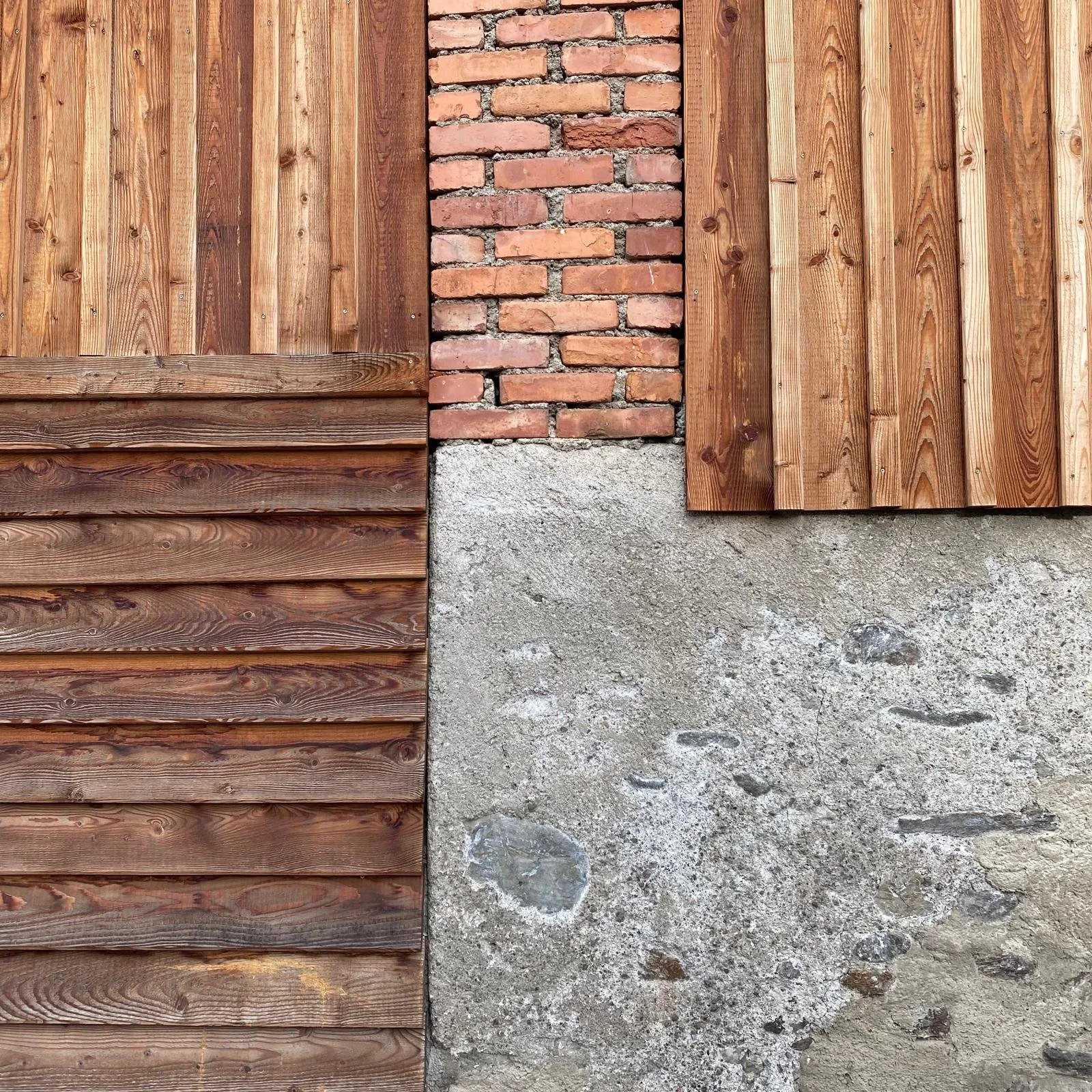 A wall with a combination of wood planks, red bricks, and concrete blocks.