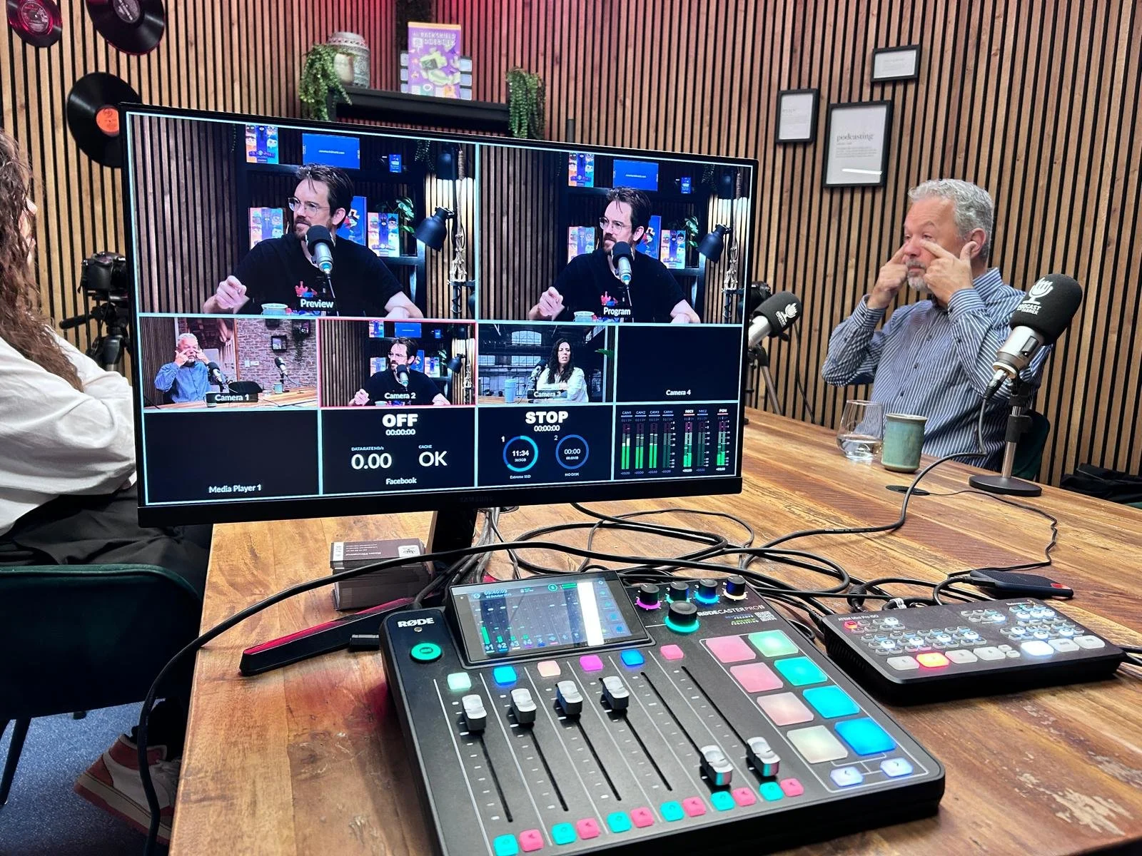 Four men sitting around a table with microphones, engaging in a podcast or interview, with a city skyline visible through large windows in the background.