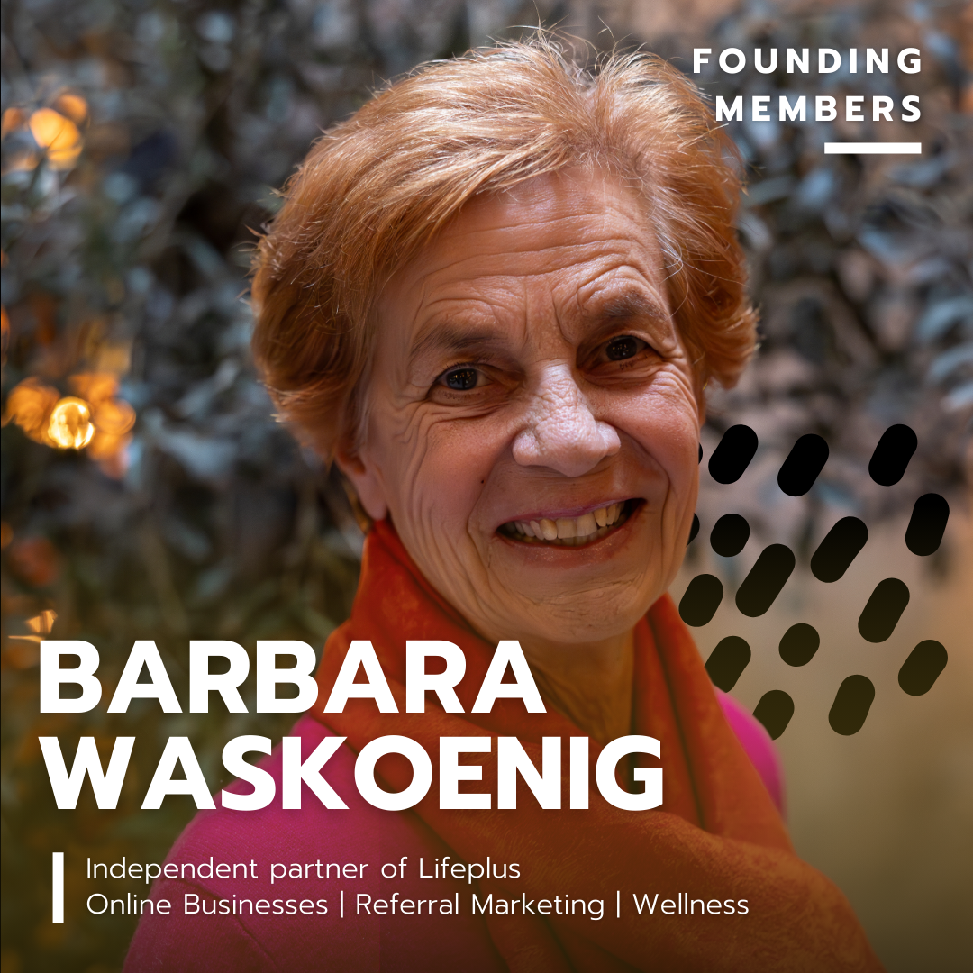 Image of an elderly woman smiling with short red hair, wearing a pink top and reddish scarf, standing outdoors near bushes with blurred lights.