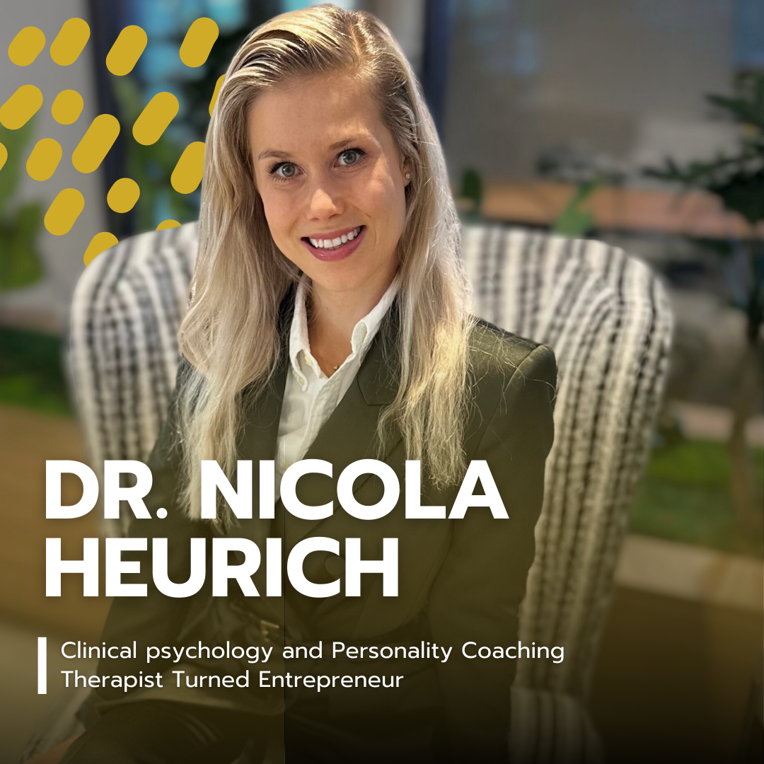 Portrait of Dr. Nicola Heurich, a woman with long blonde hair, wearing a dark blazer and white shirt, smiling while seated in a wicker chair with a patterned cushion, in a well-lit indoor setting with plants and blurred background.