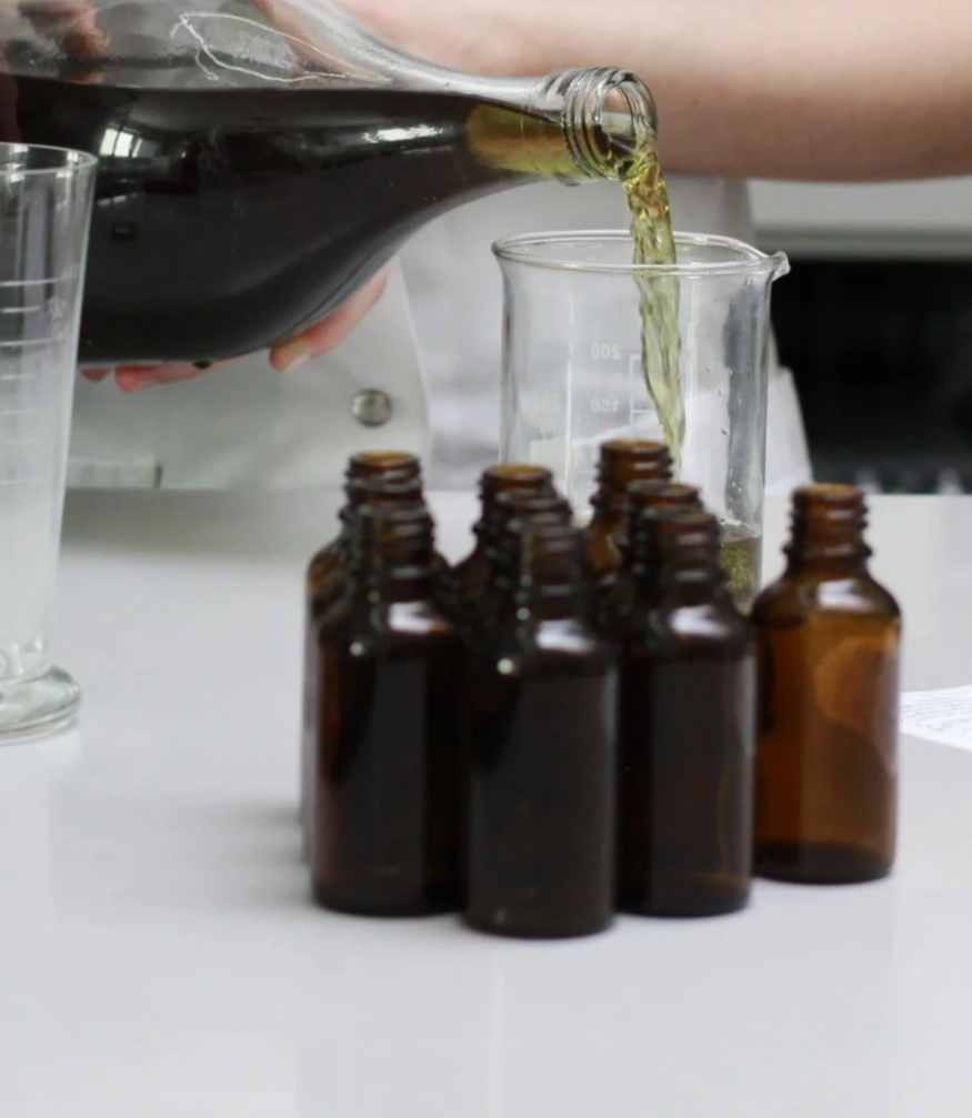 Ein Laborbild mit Braunglasflaschen, in denen wahrscheinlich Arzneimittel oder Chemikalien aufbewahrt werden, und eine Person, die eine dunkle Flüssigkeit in ein Reagenzglas gießt.