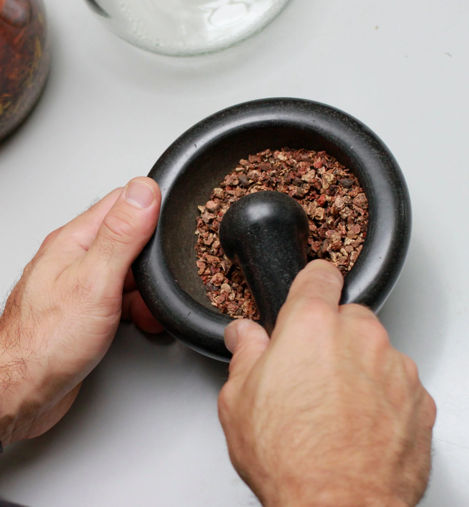 Person, die getrocknete Gewürzkräuter im Mörser zerreibt.