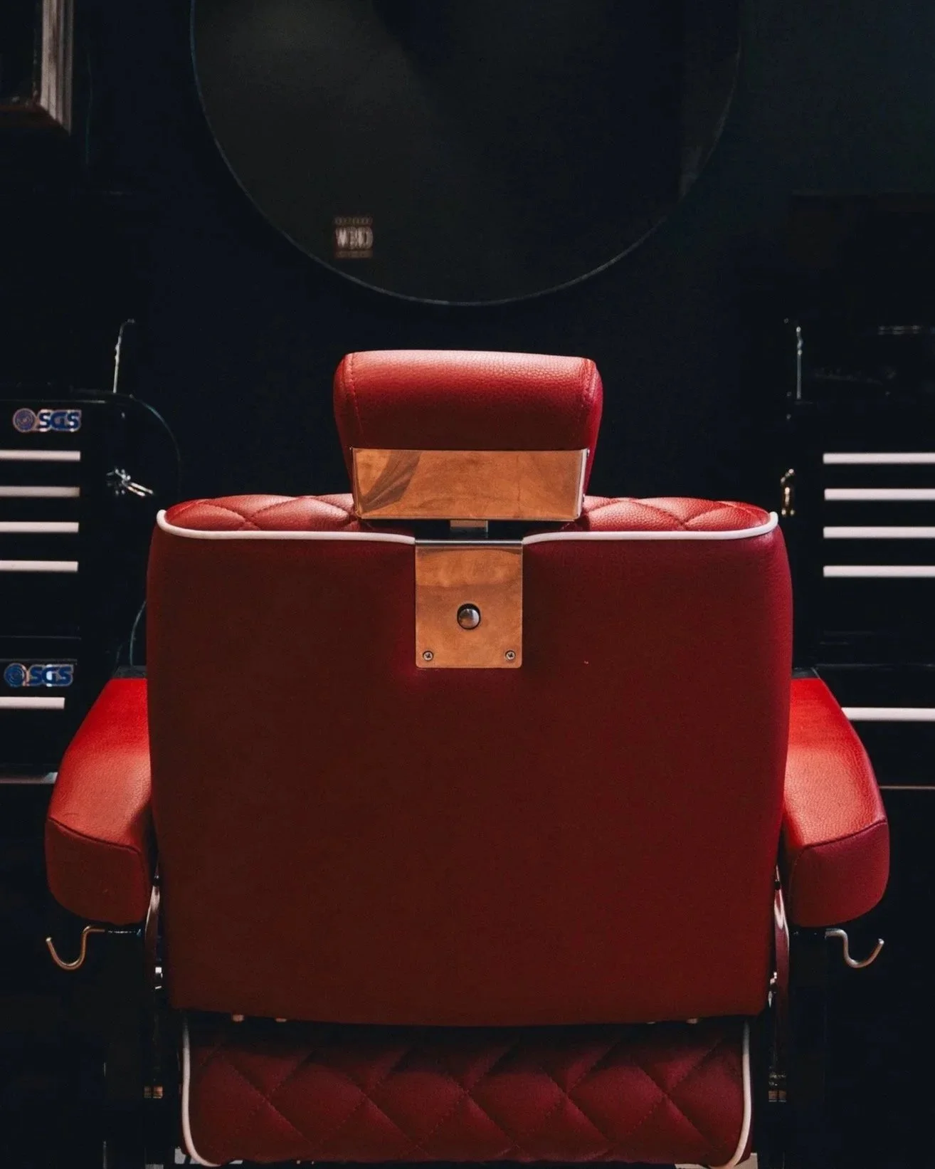 A red barber chair is positioned in front of dark walls with barber tools and equipment visible on the sides.