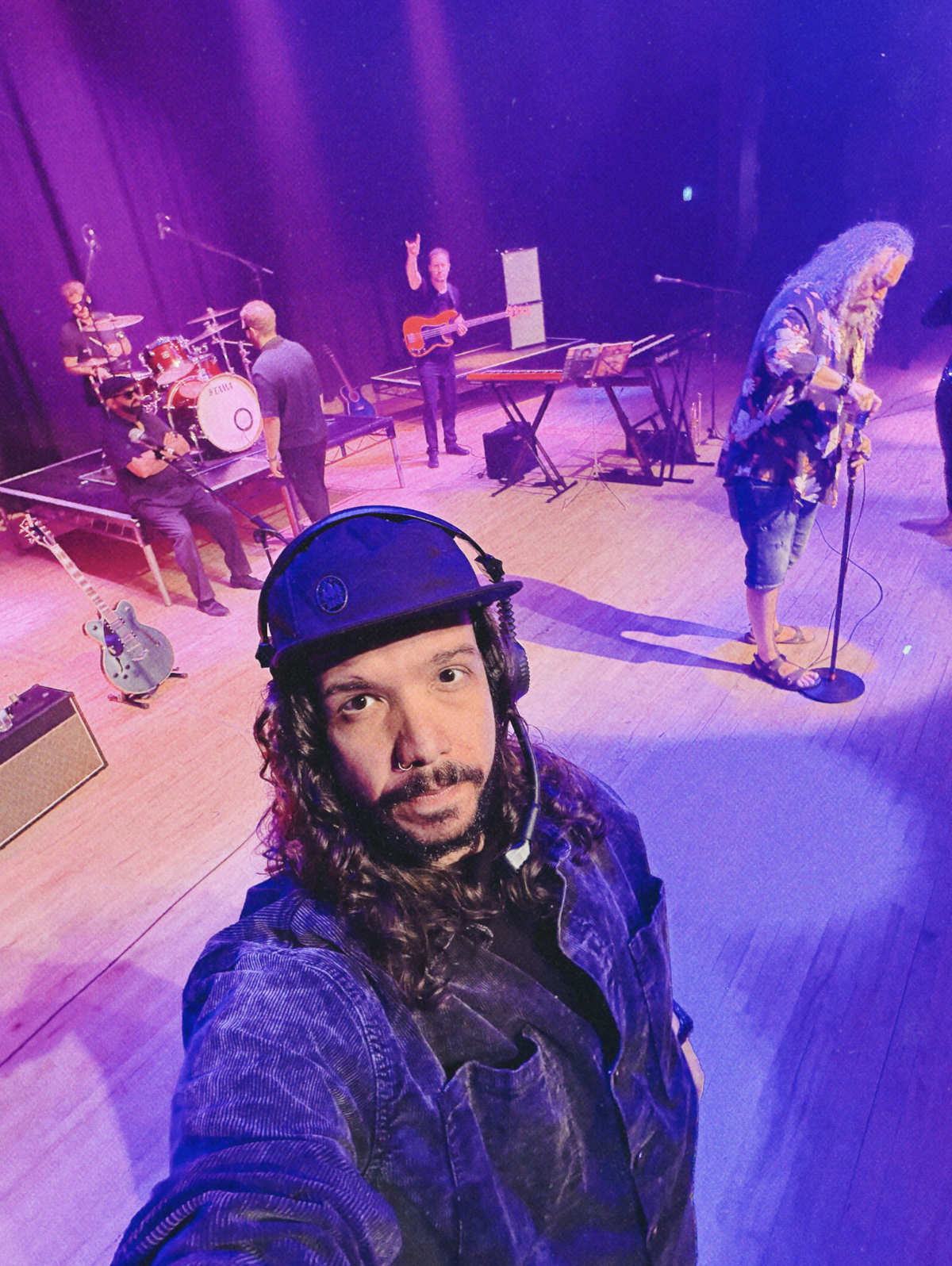 Dan, lead videographer and director, on set during a live music video shoot, with band members rehearsing on stage in purple lighting behind him.